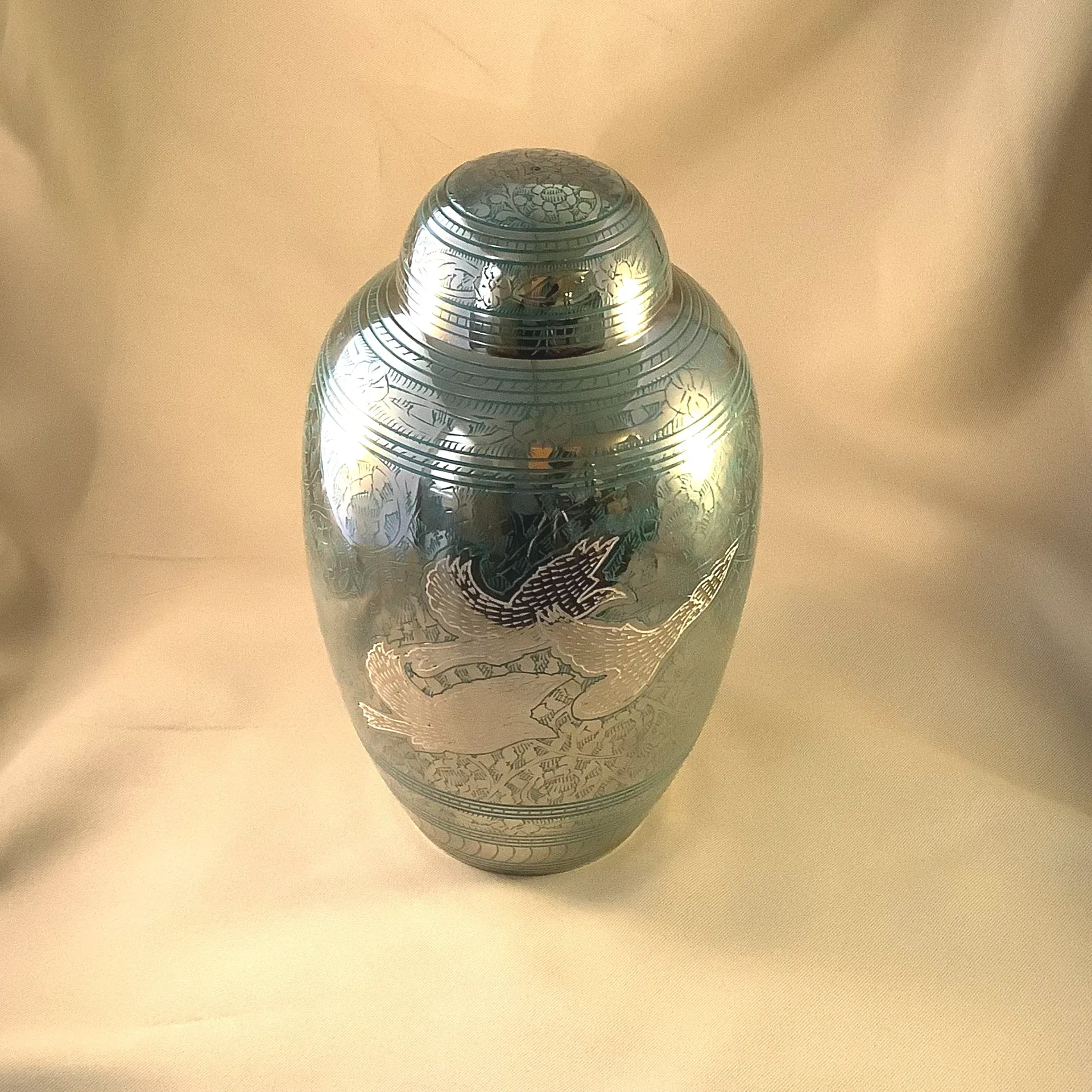 Silver decorative urn with engraved floral patterns on a beige cloth background