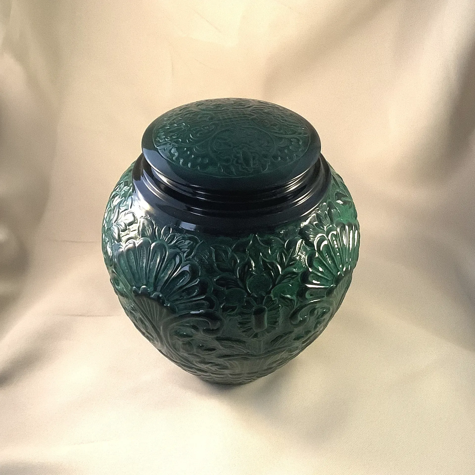 Green embossed glass jar with a dark lid on a light fabric background