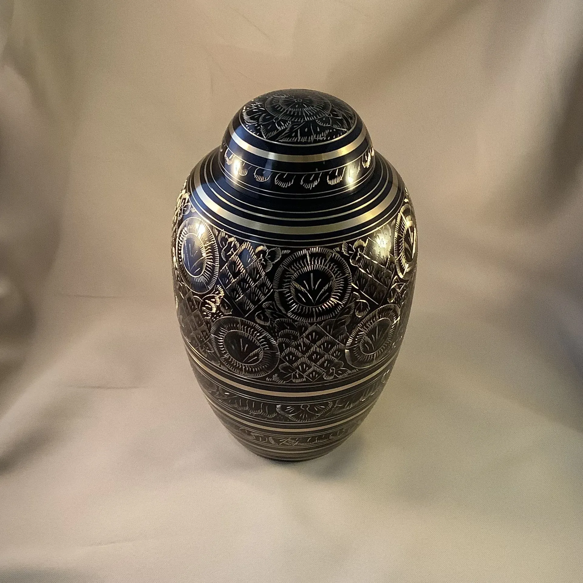 Ornate blue-and-silver decorative vase with intricate patterns on a neutral fabric background