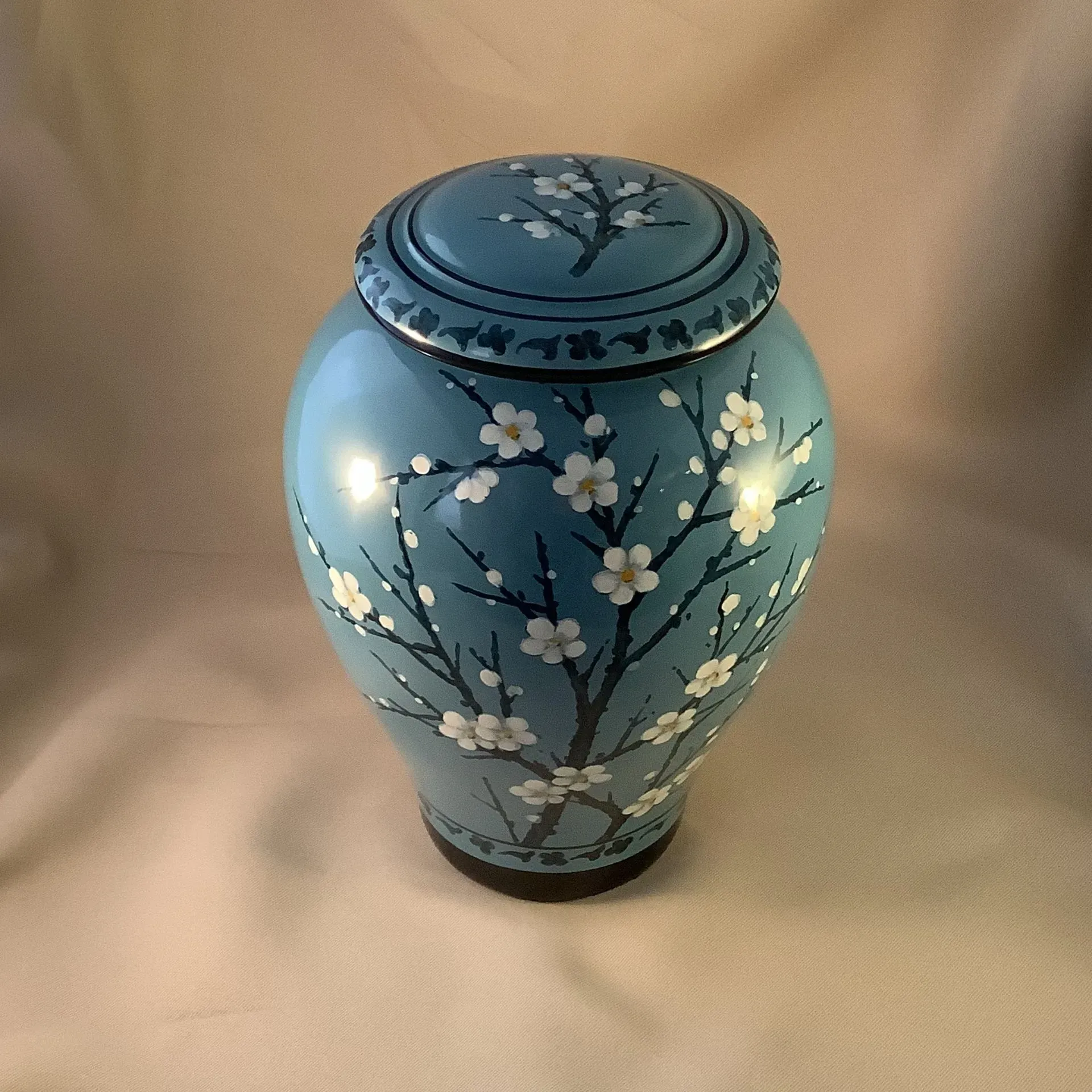 Blue ceramic jar with white floral blossom design and matching lid on a neutral background