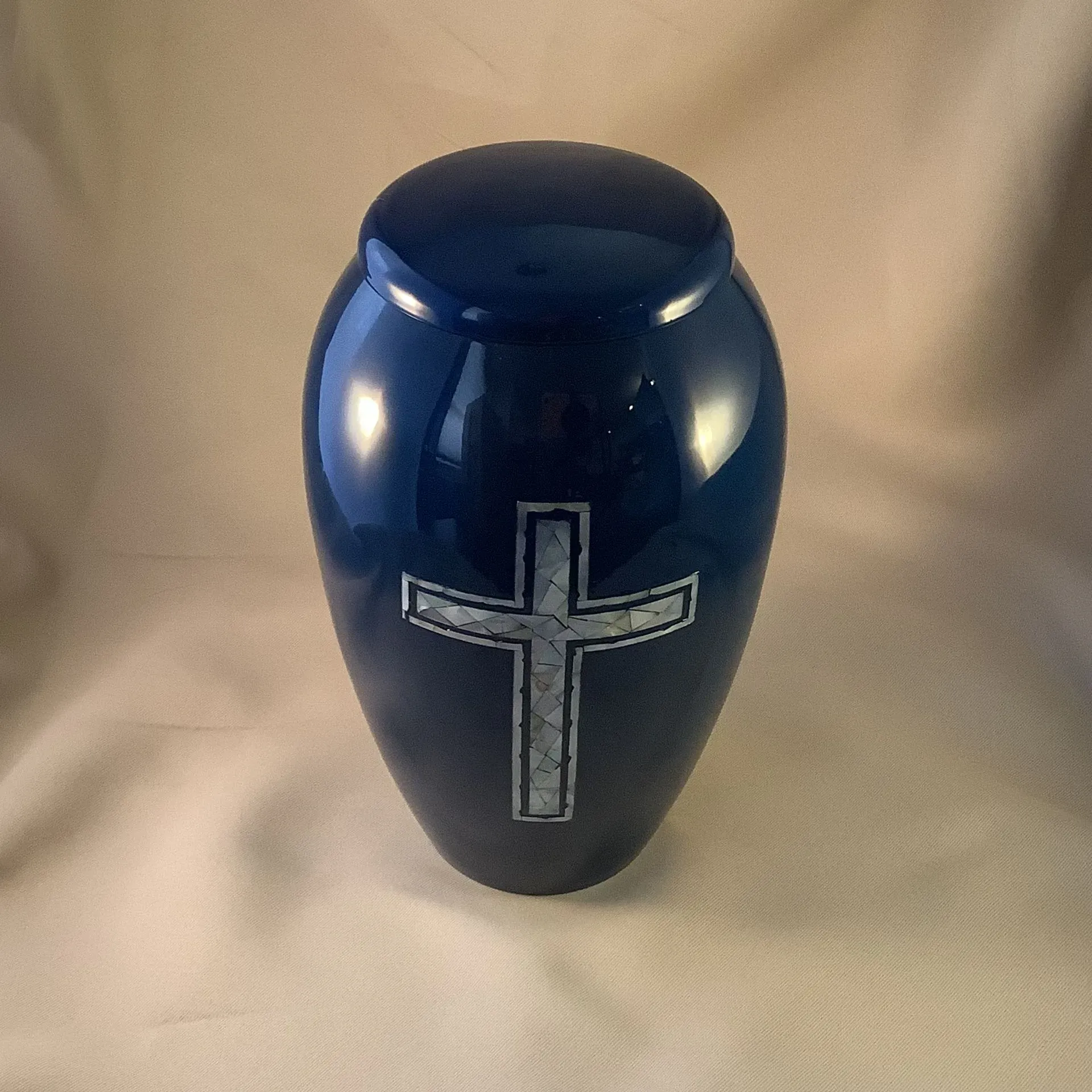 Dark blue urn with a silver cross on the front against a beige background