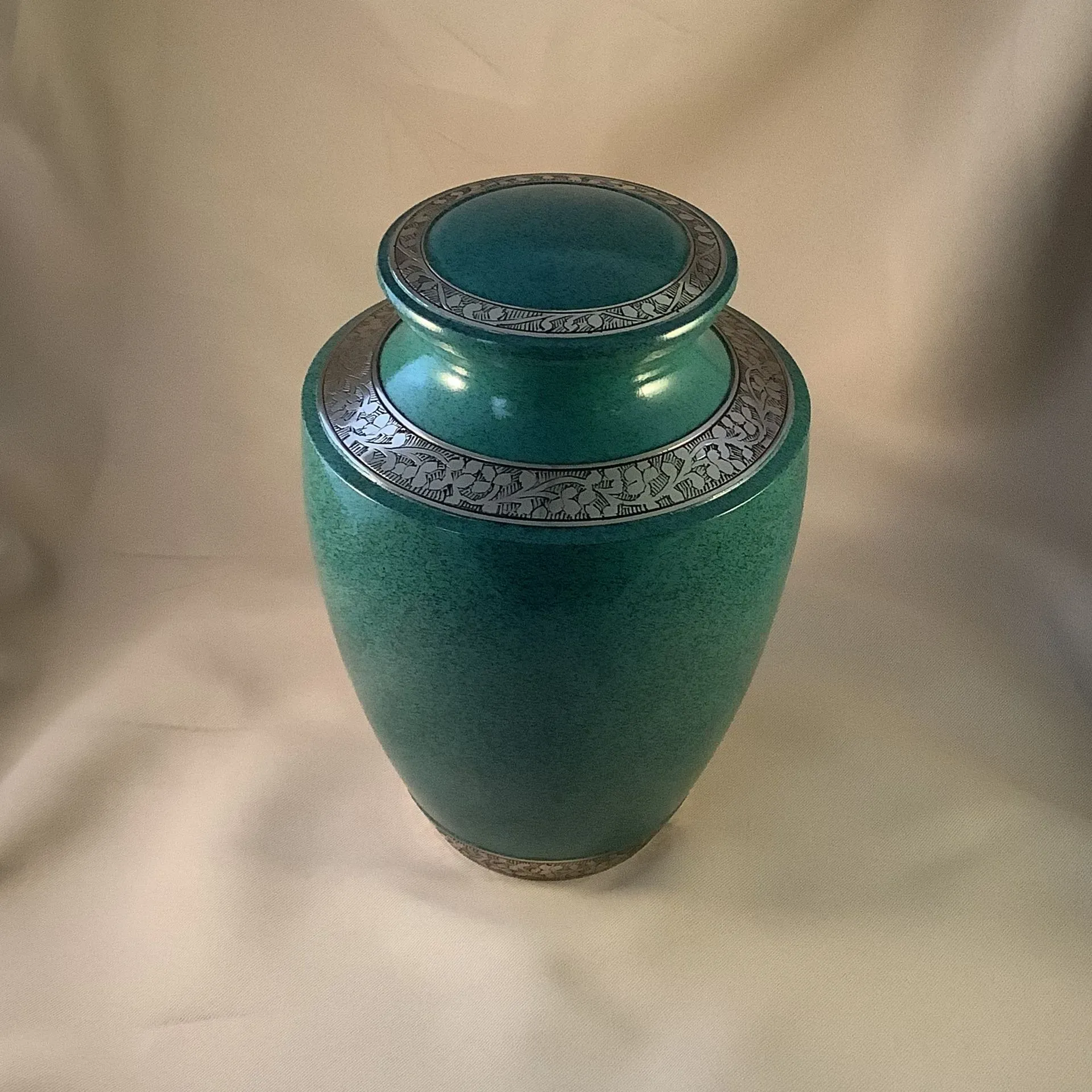 Turquoise ceramic vase with silver decorative bands on a beige fabric background