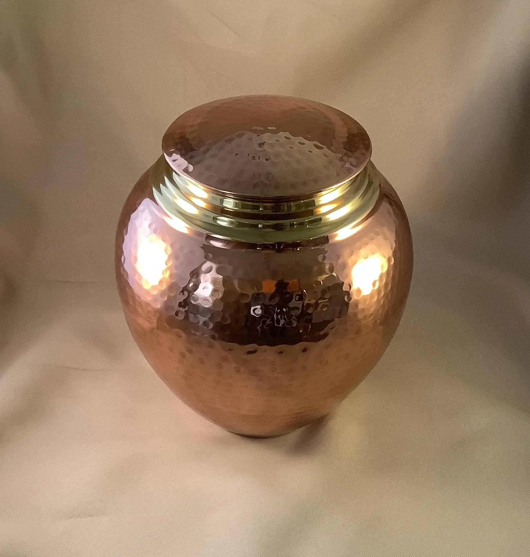 Copper urn-shaped jar with a round lid on a beige background