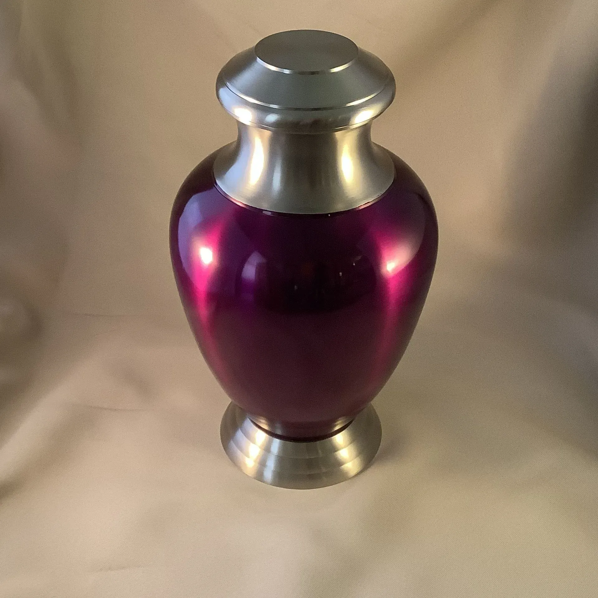Purple glass vase with silver metal top and base on a beige background