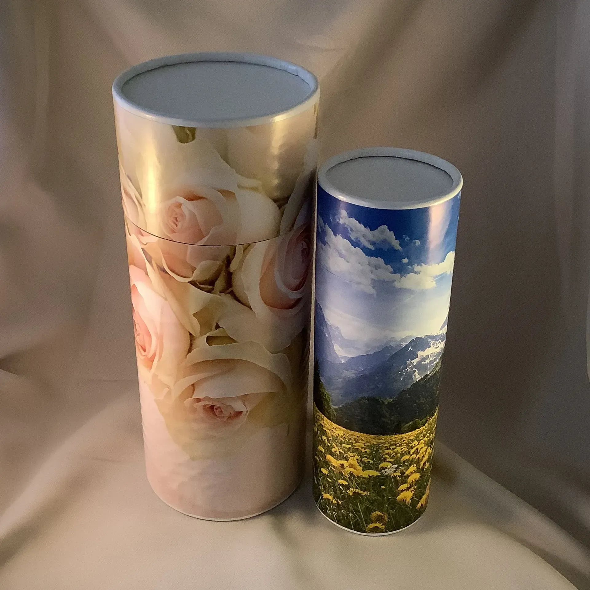 Two decorative cylindrical canisters, one tall with pale roses and one shorter with a mountain and flower scene.