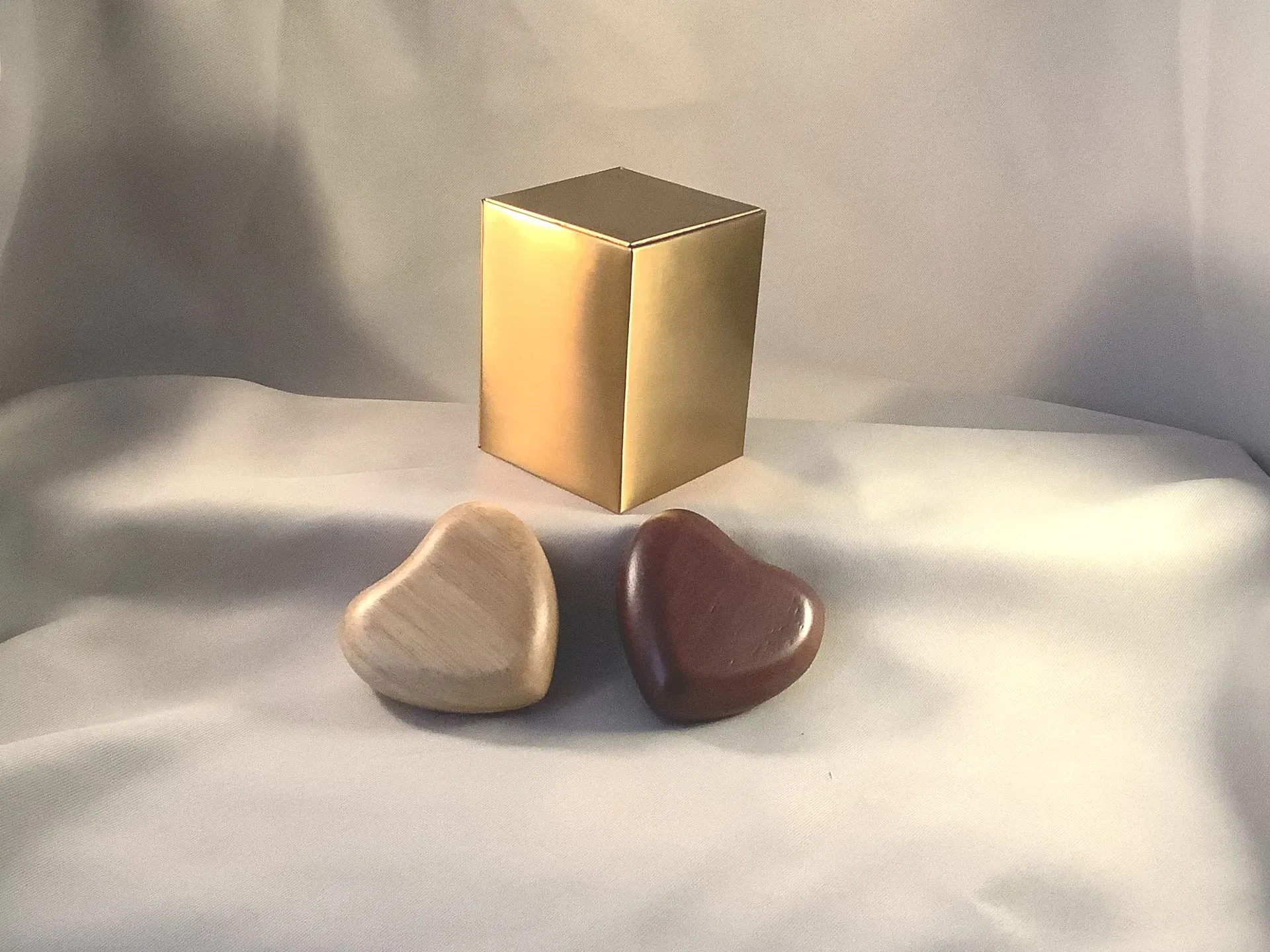 Gold box behind two heart-shaped stones on white fabric.