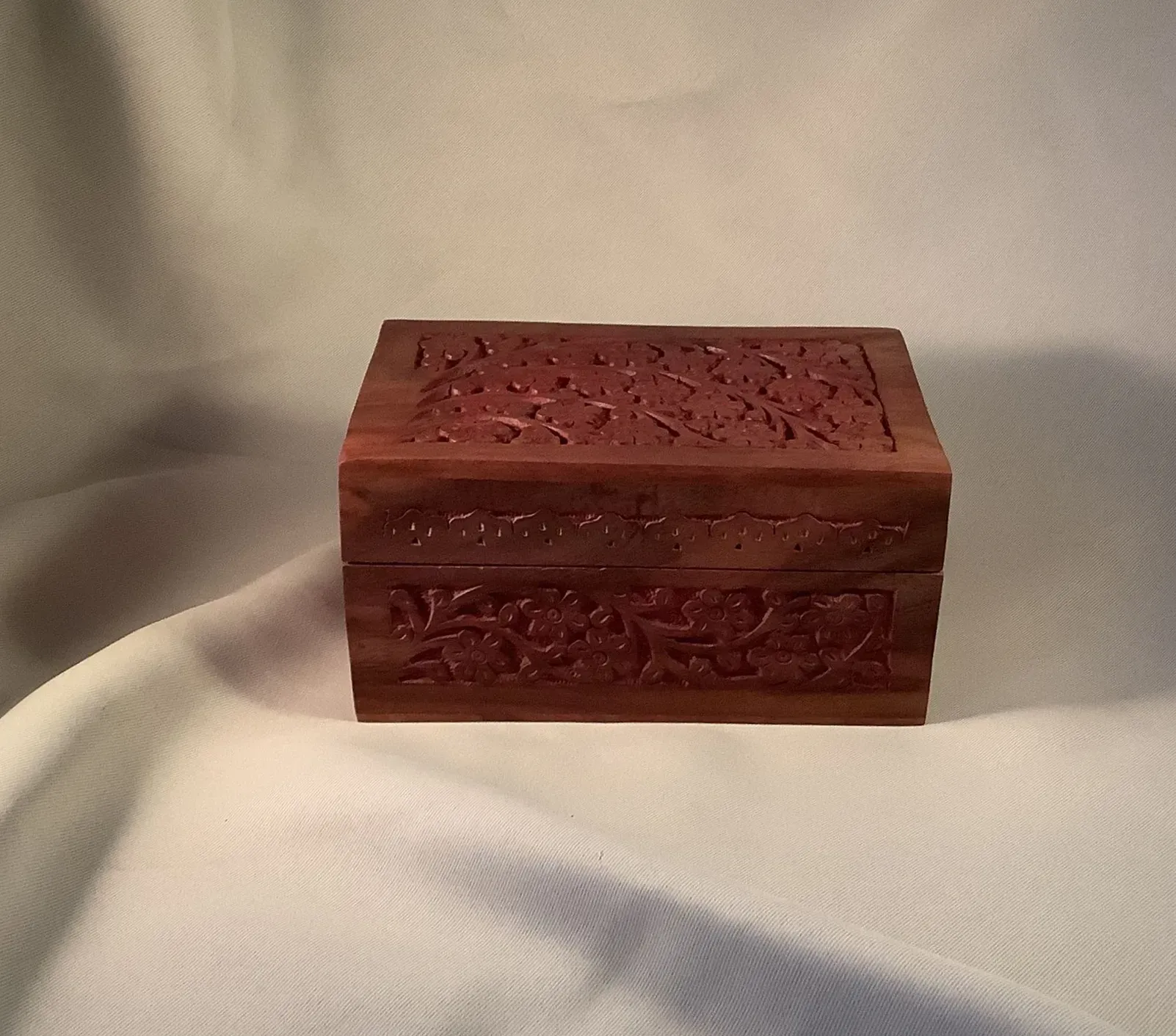 Small carved reddish-brown wooden box on a light fabric background