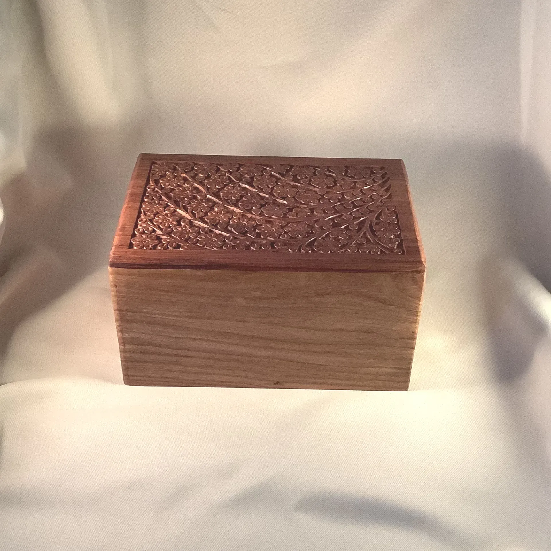 Wooden decorative box with an ornate carved lid on a light fabric background