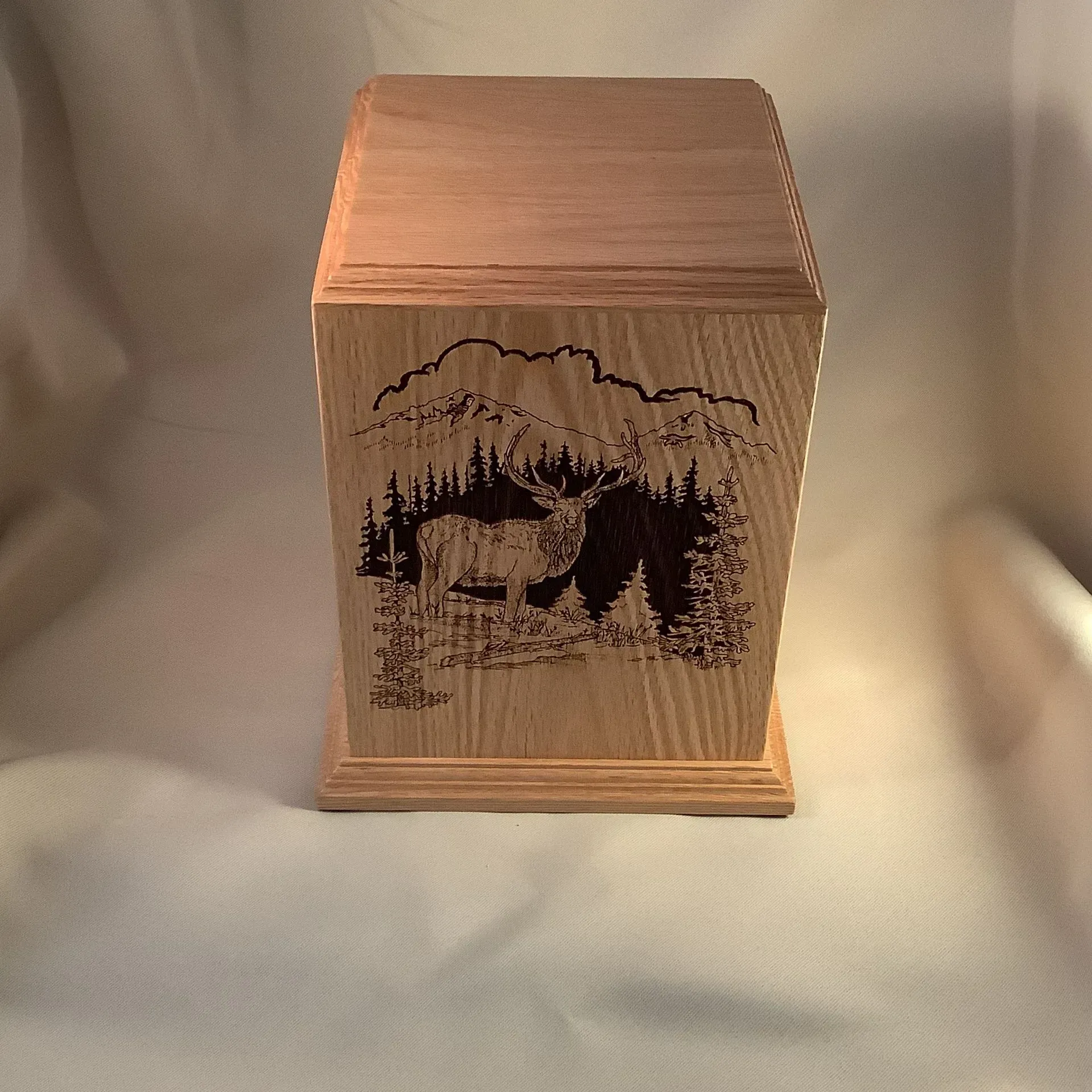 Wooden box with a carved wildlife scene of a deer in a forest, lit warmly against a plain background