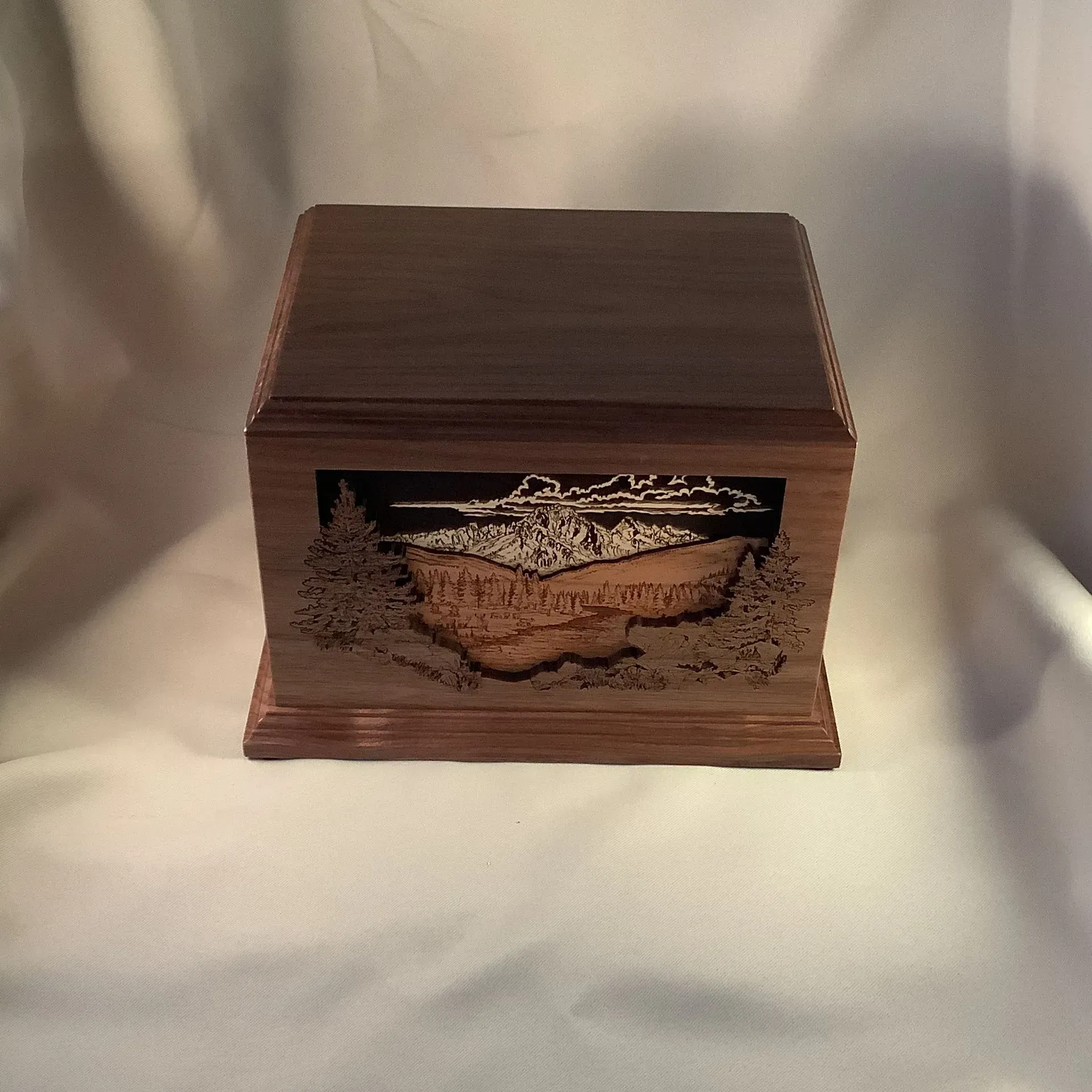 Wooden box with a decorative front plaque, centered against a draped white background