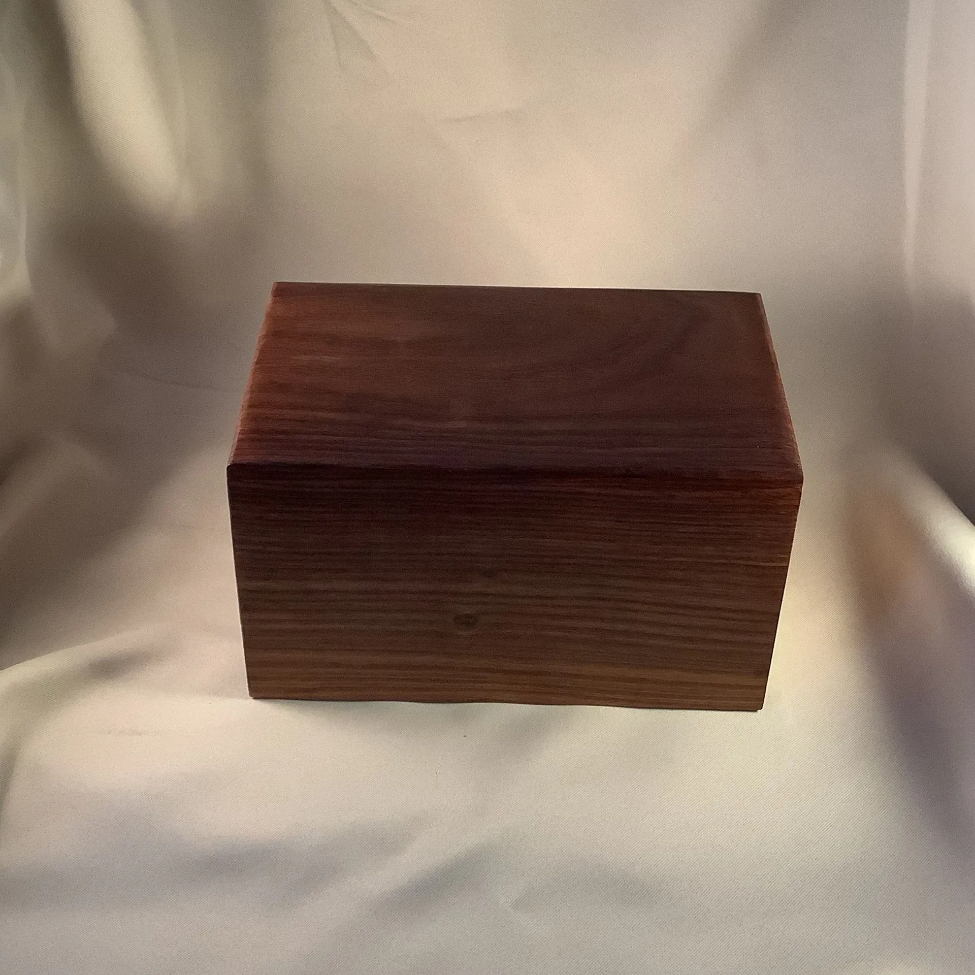 A dark wooden rectangular box on a light draped fabric background.