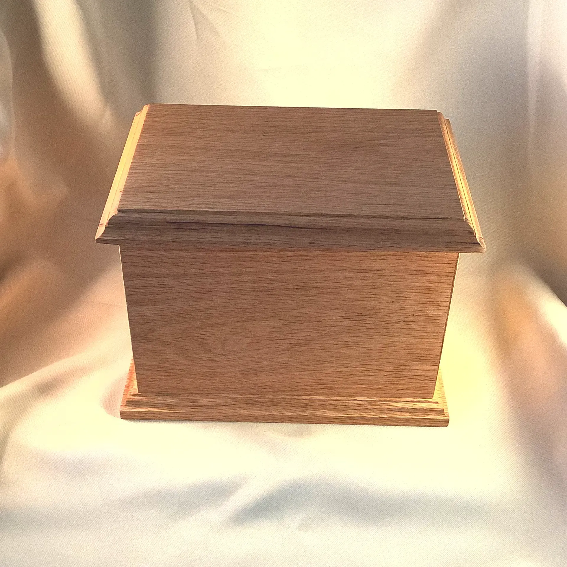 Small wooden box with a slanted lid on a light fabric background