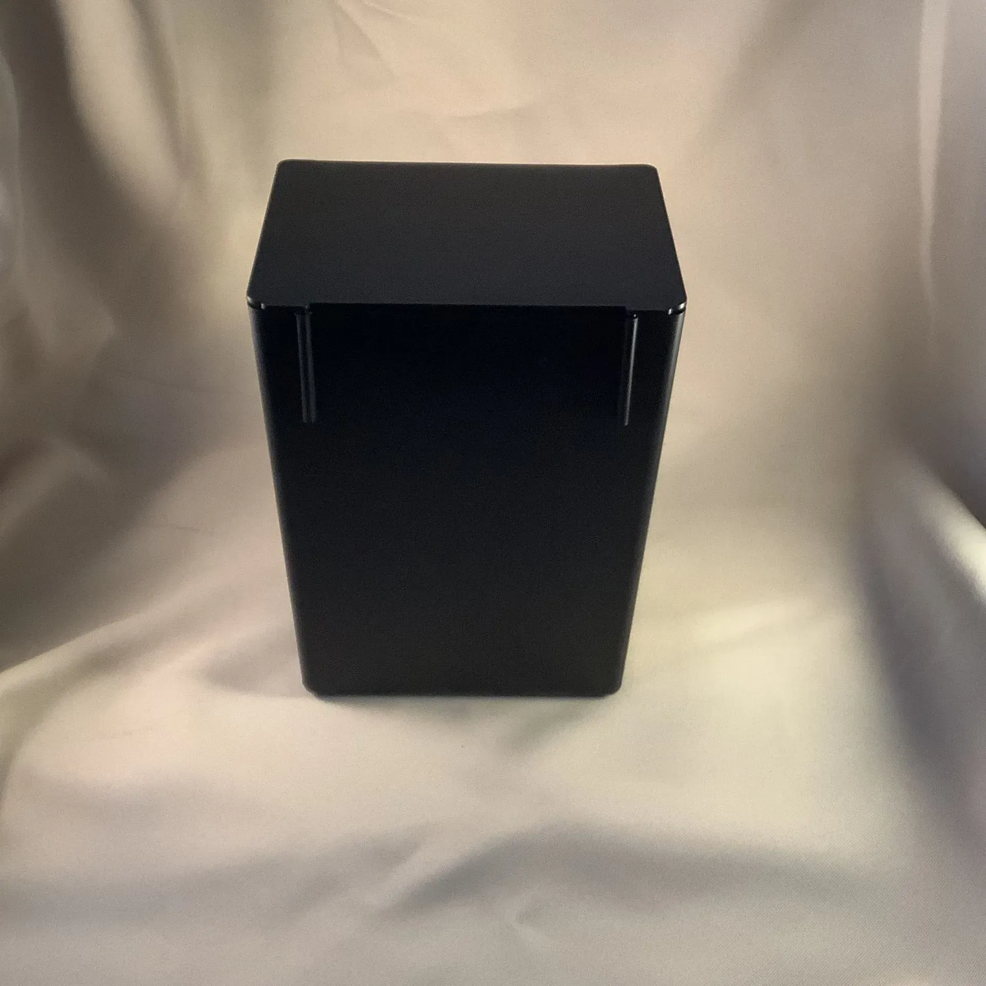 Black rectangular box with a hinged lid on a white draped background