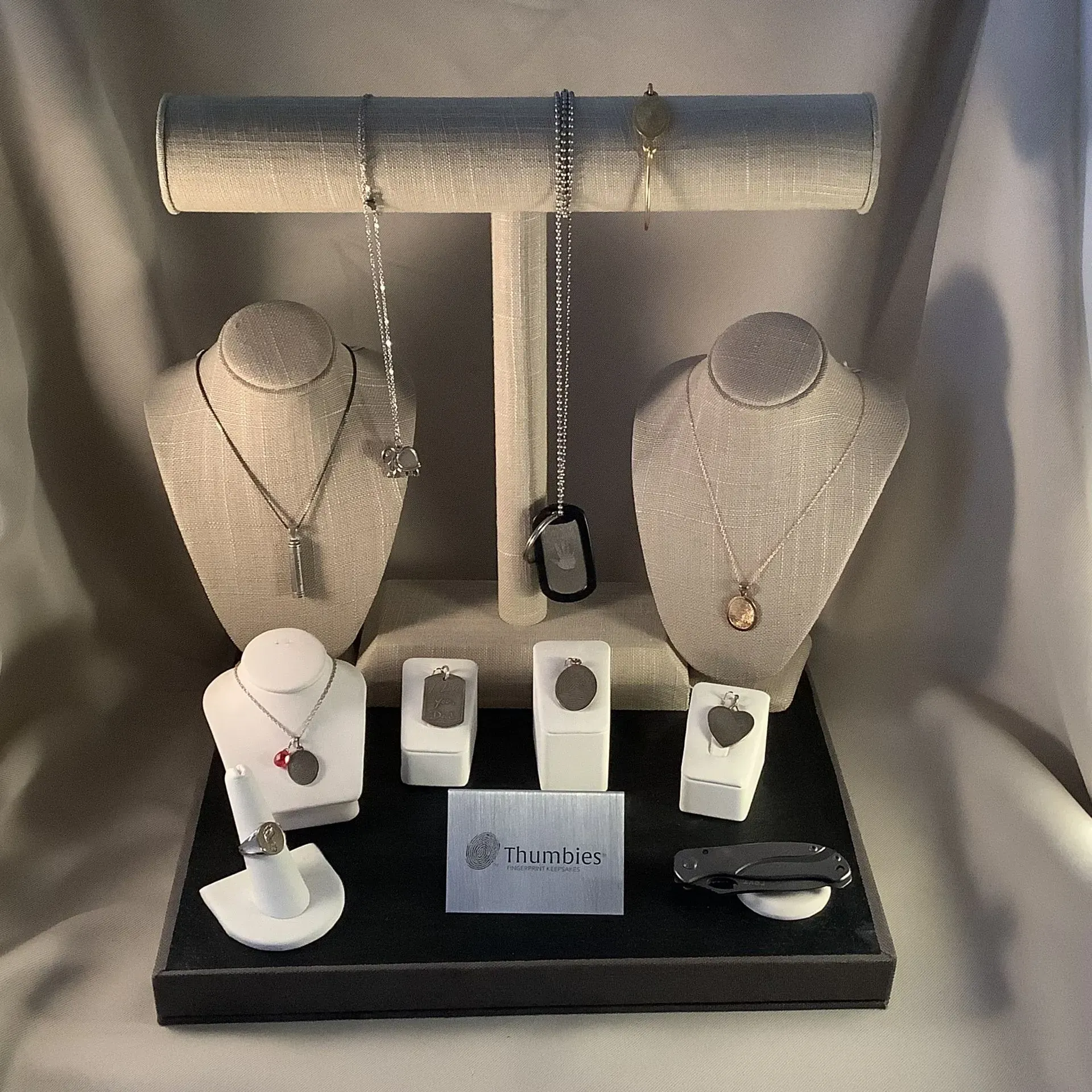 Jewelry display with necklaces and rings on white stands against a gray backdrop