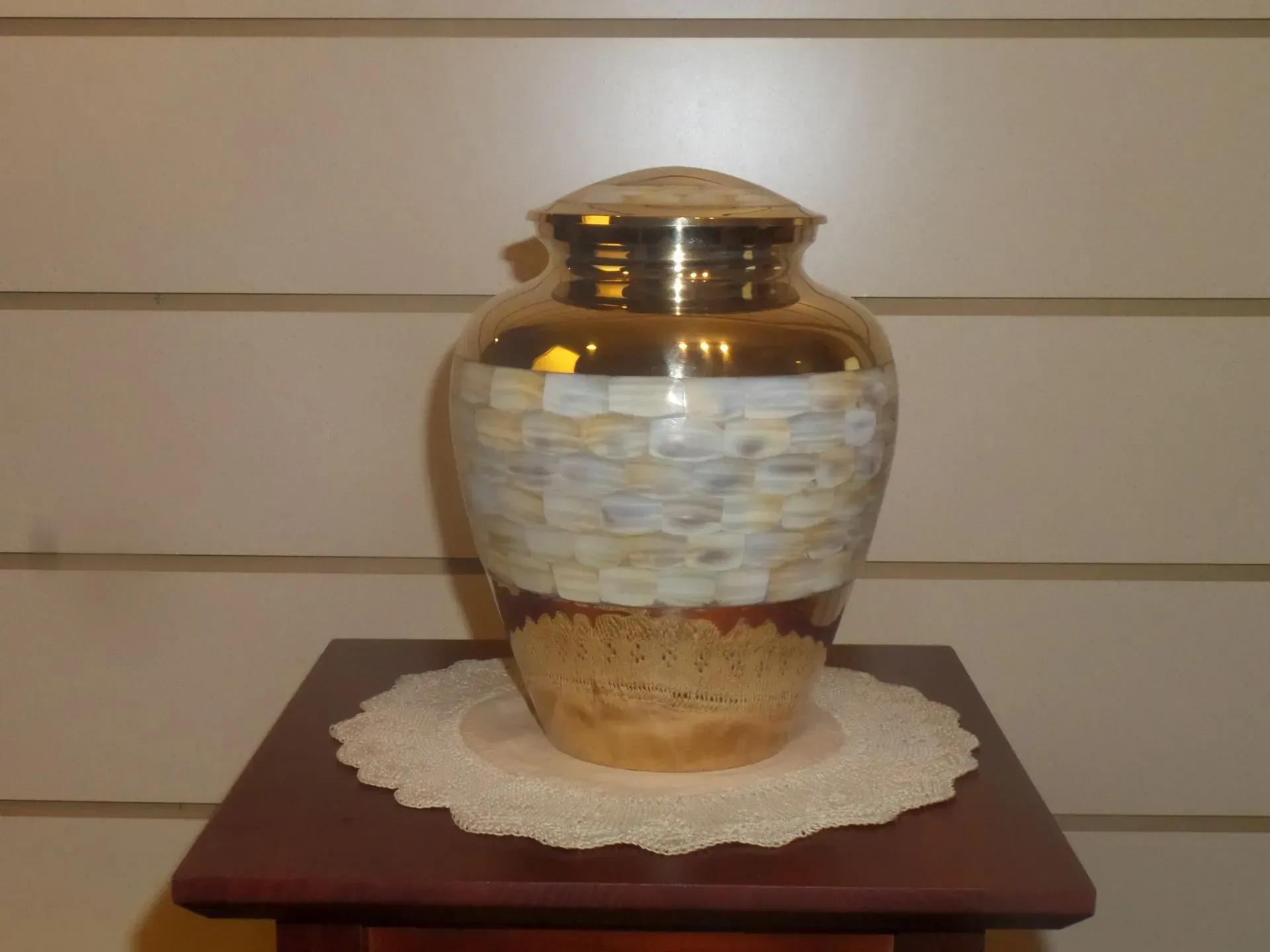 Decorative gold-and-cream urn on a lace doily atop a wooden table