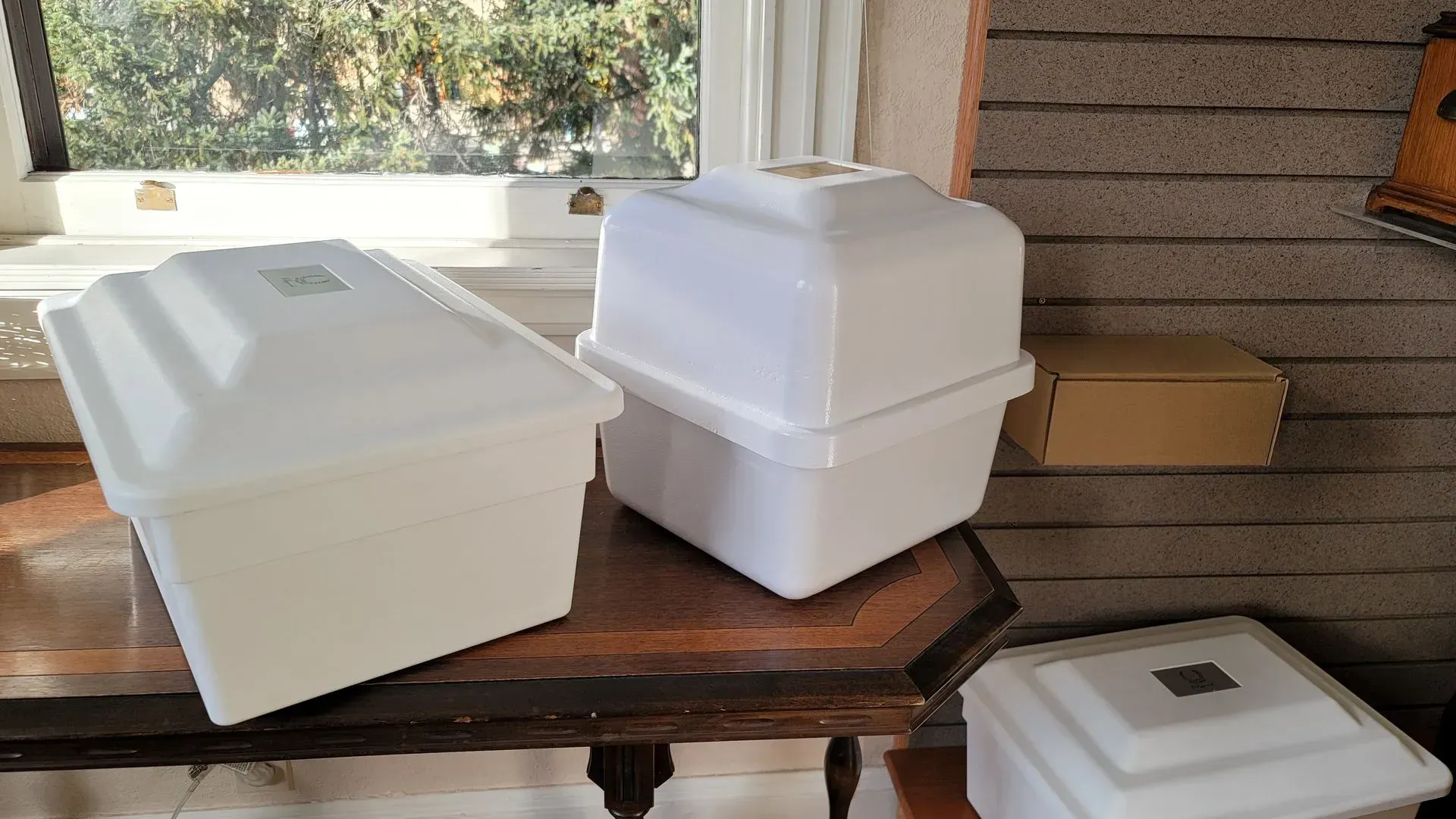 Three white urn vaults on a wooden table by a window.