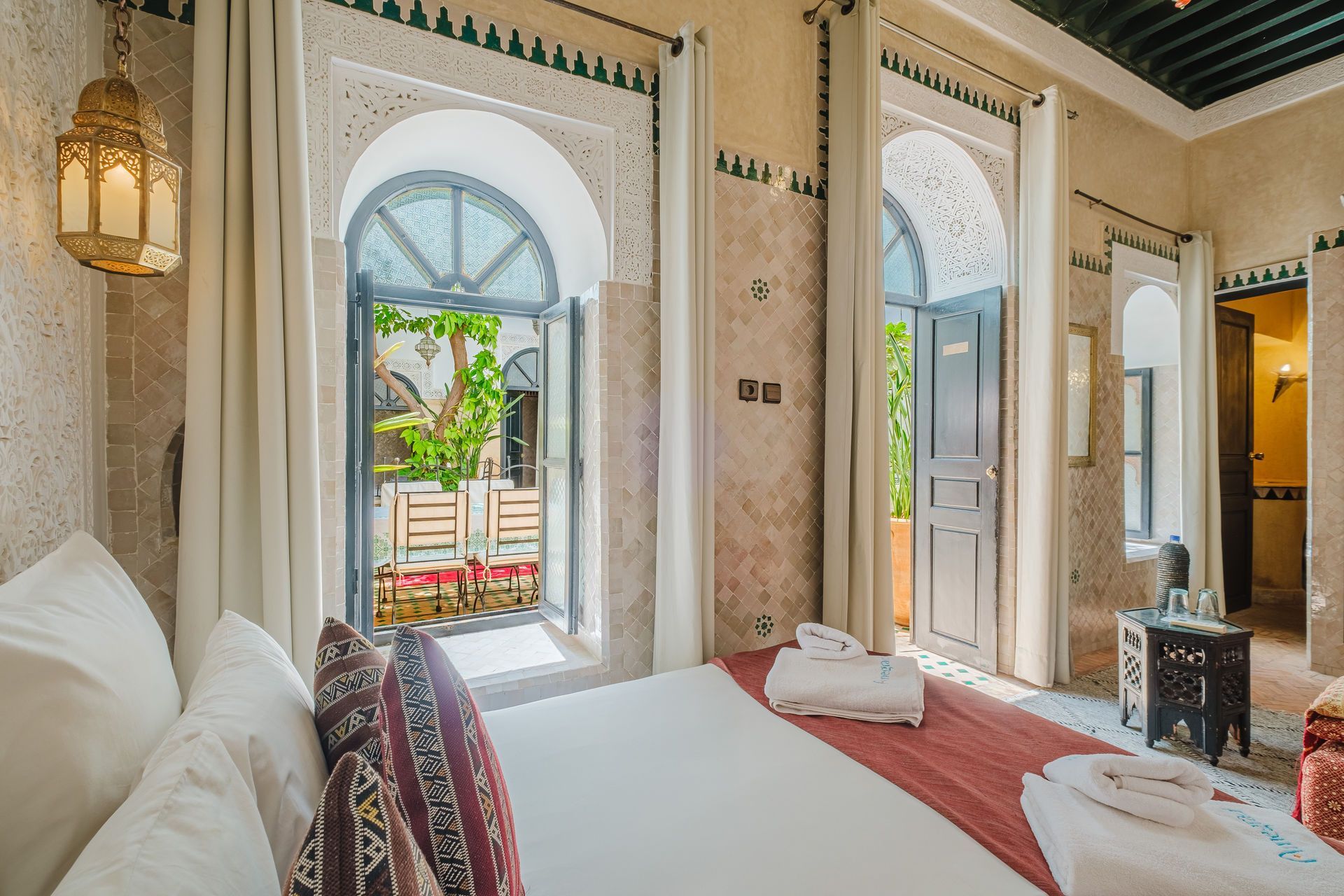 Bedroom with arched doorway leading to courtyard, ornate decor, white bedding, red accents.