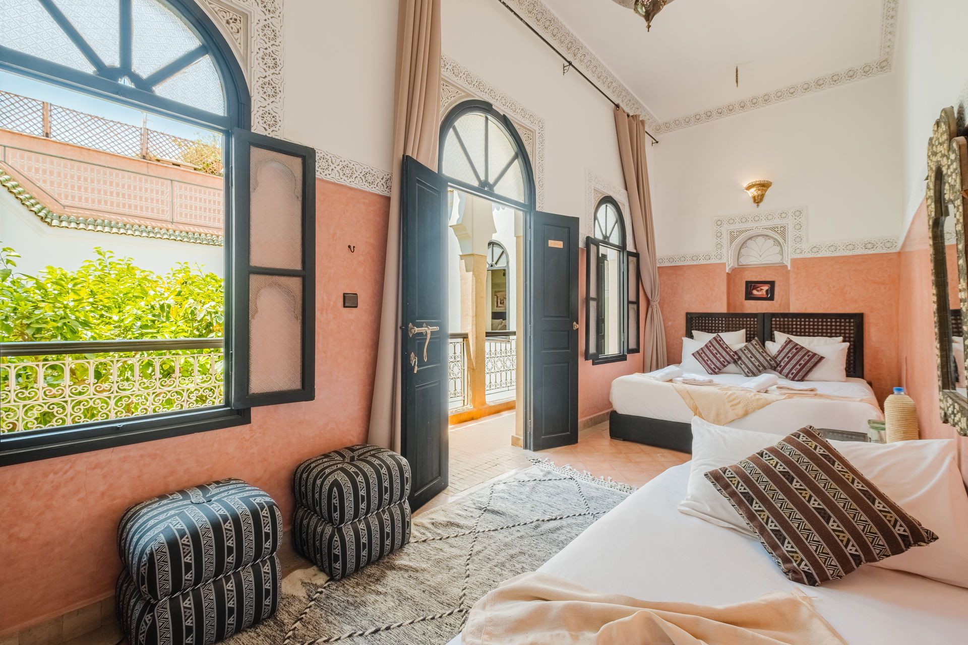 A hotel room in Morocco with open balcony door, two beds, and decorative seating.
