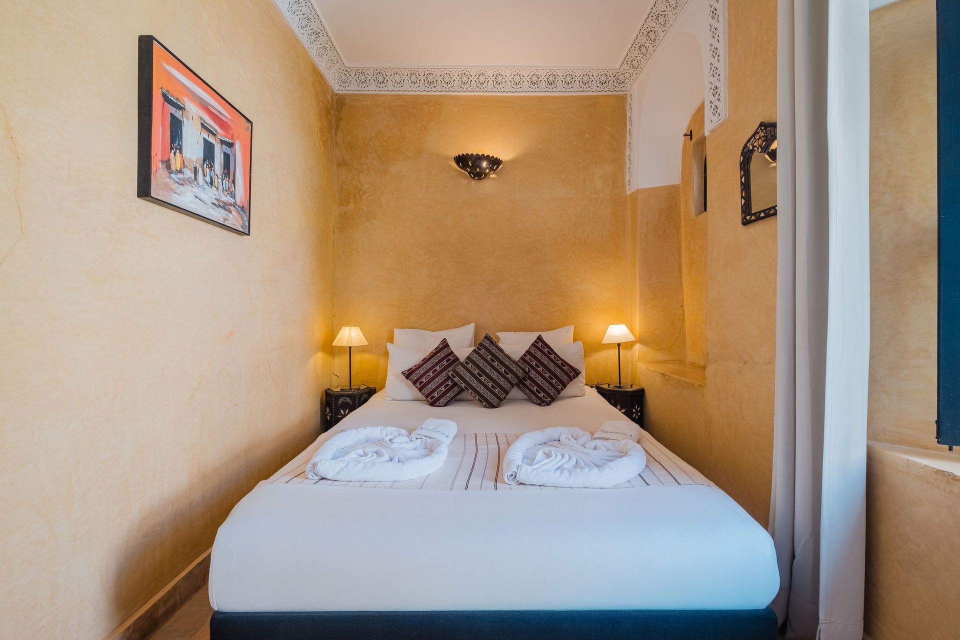 Small hotel bedroom with a double bed, two bedside tables, and artwork on the wall.