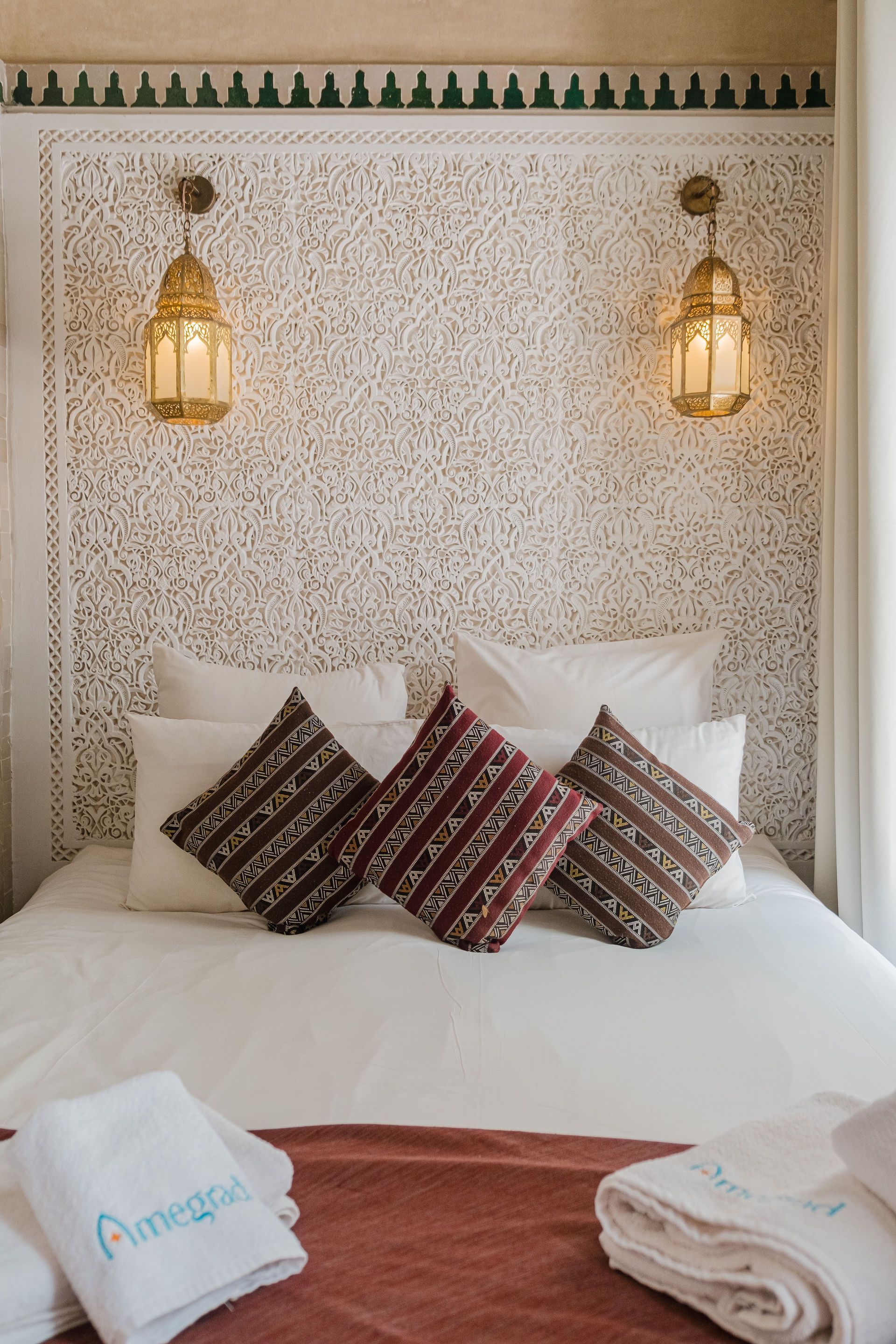 Bedroom with white carved headboard, gold lanterns, white bedding, patterned pillows, and red accents.