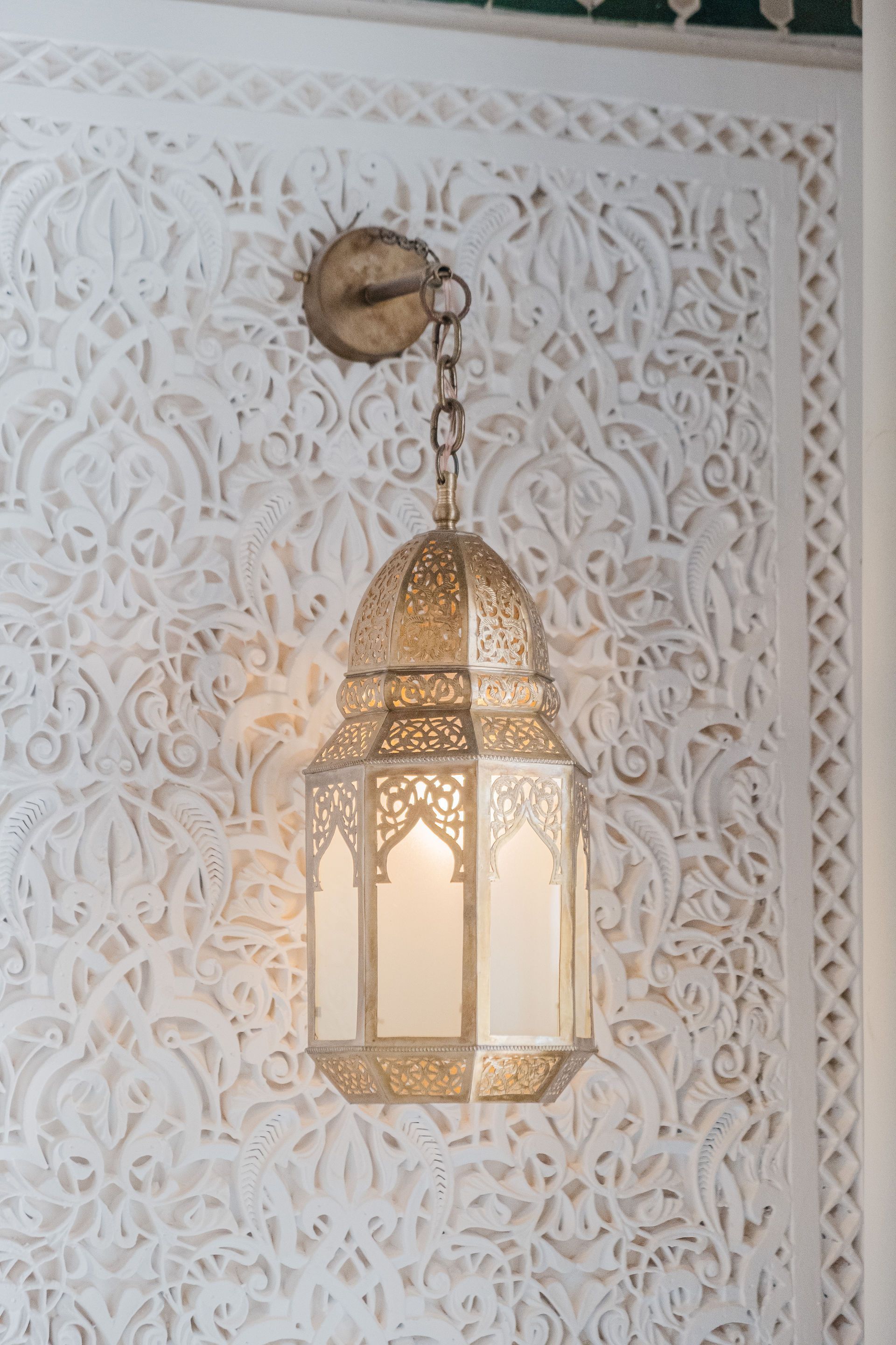 Ornate gold lantern hanging against a white, carved wall in a Middle Eastern setting.