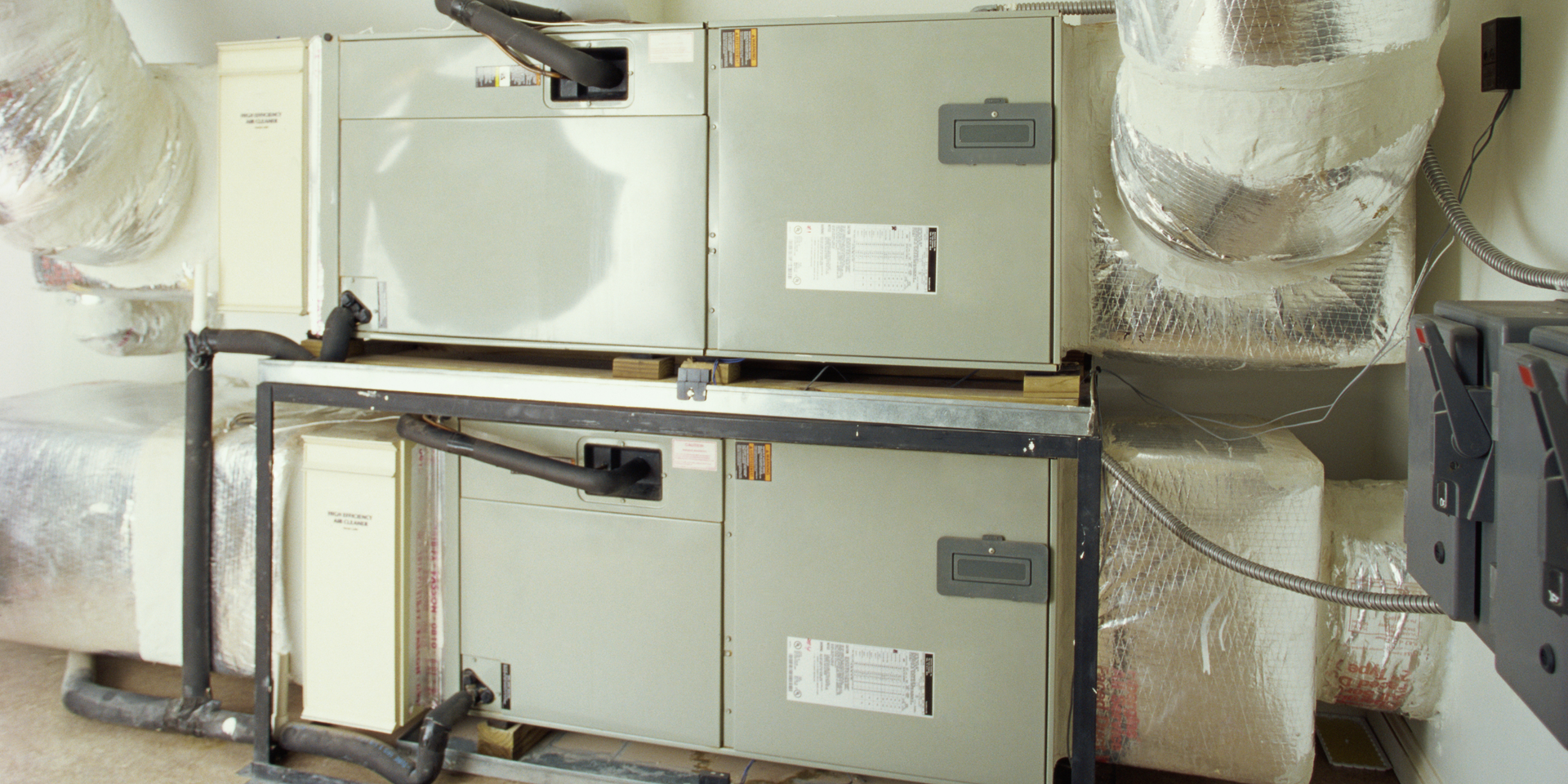 Two wall-mounted HVAC units with insulated ducts and piping in a mechanical room