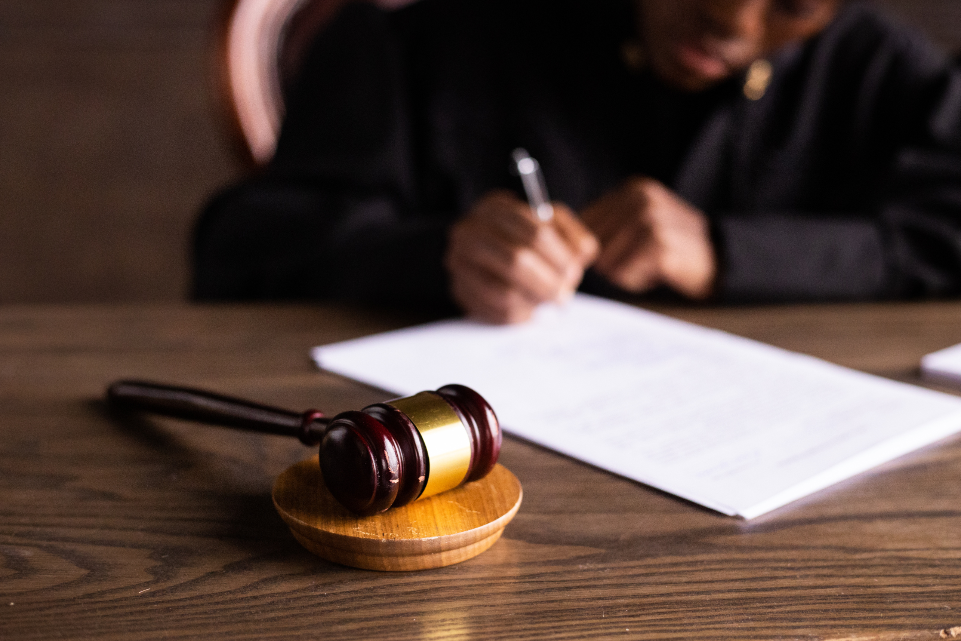 Judge’s gavel on a wooden desk beside a person signing a document