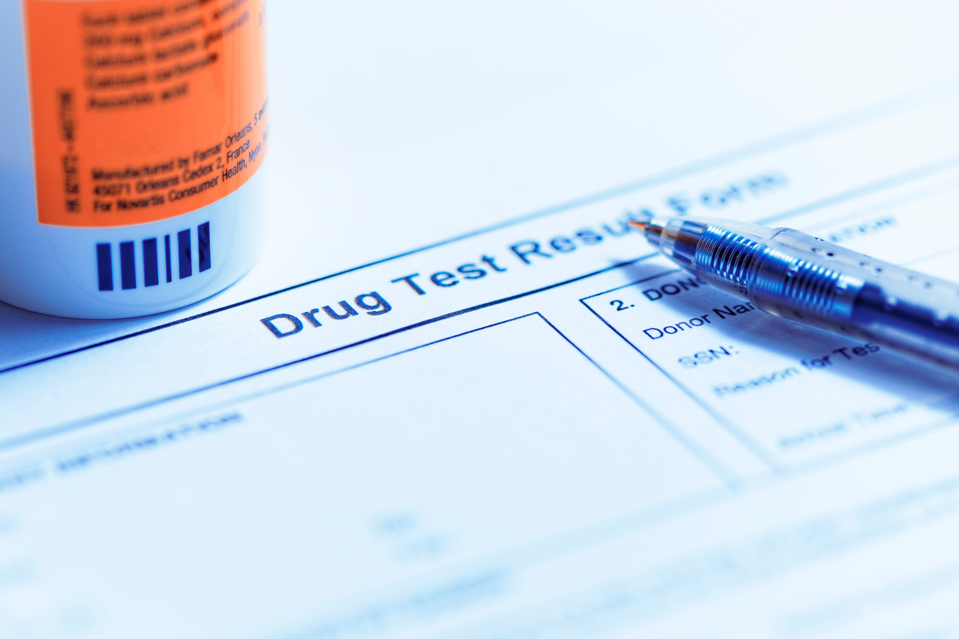 Drug test results form with a pill bottle and a blue pen on a desk