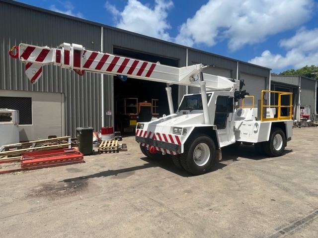 Yellow mobile crane on pavement under a blue sky, boom extended.