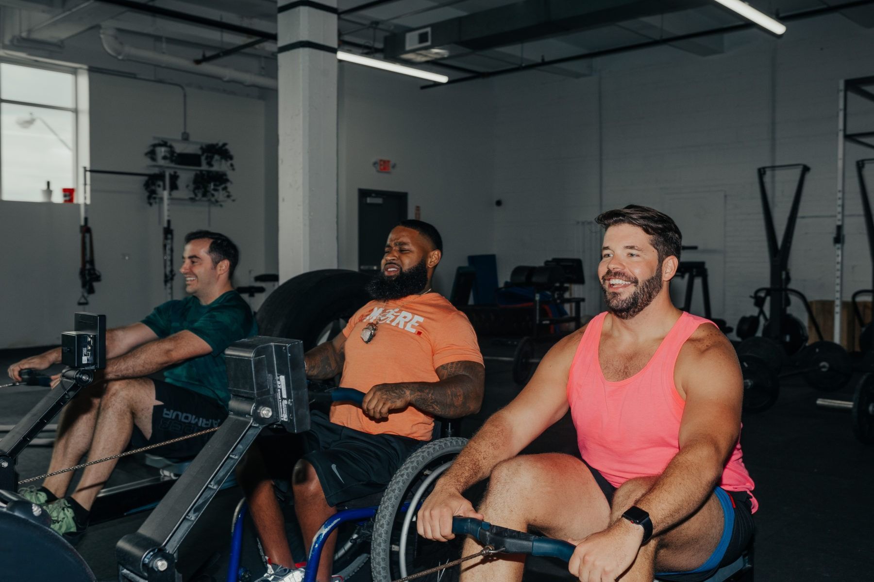 Three men are riding rowing machines in a gym.