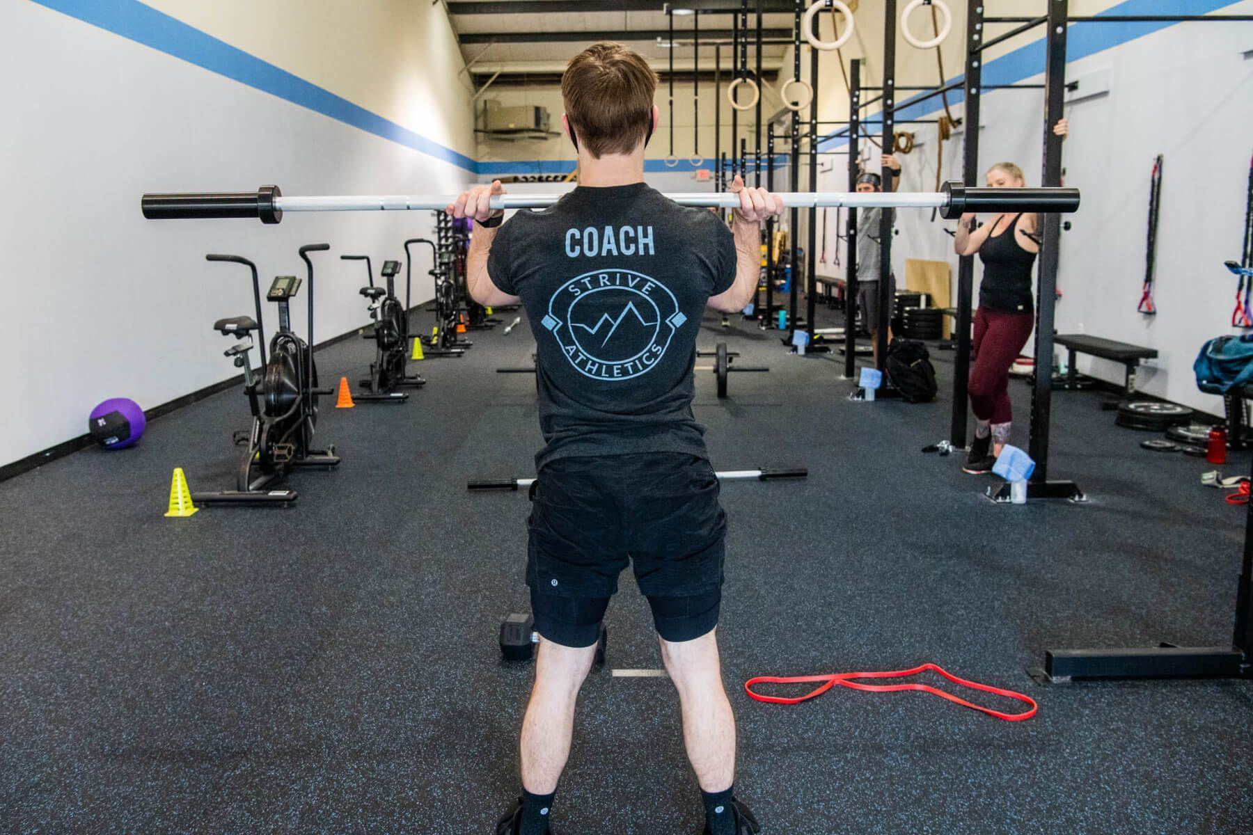A man in a coach shirt is lifting a barbell in a gym.