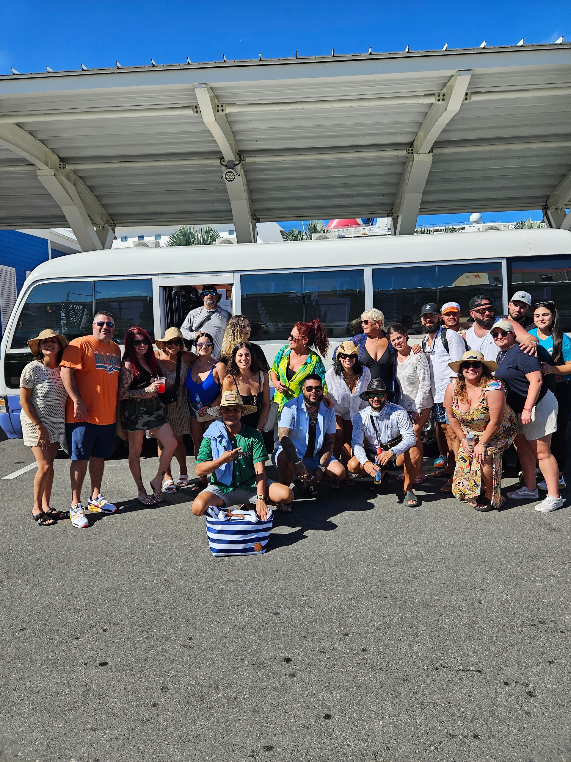 Group of people posing in front of a white bus under a canopy, sunny day.