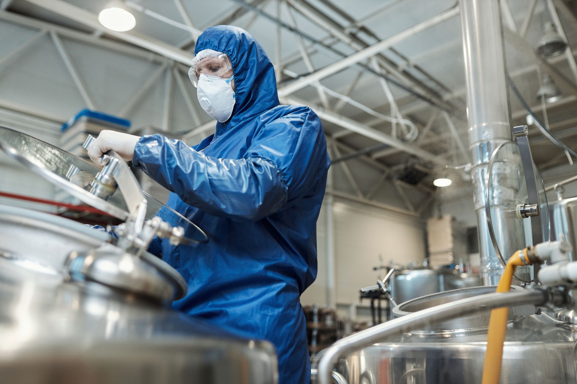 Person in blue protective suit and mask working with machinery in a factory.