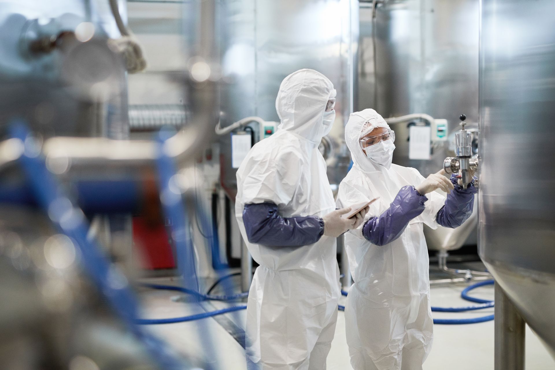 Two people in protective suits inspecting equipment in a sterile industrial facility.
