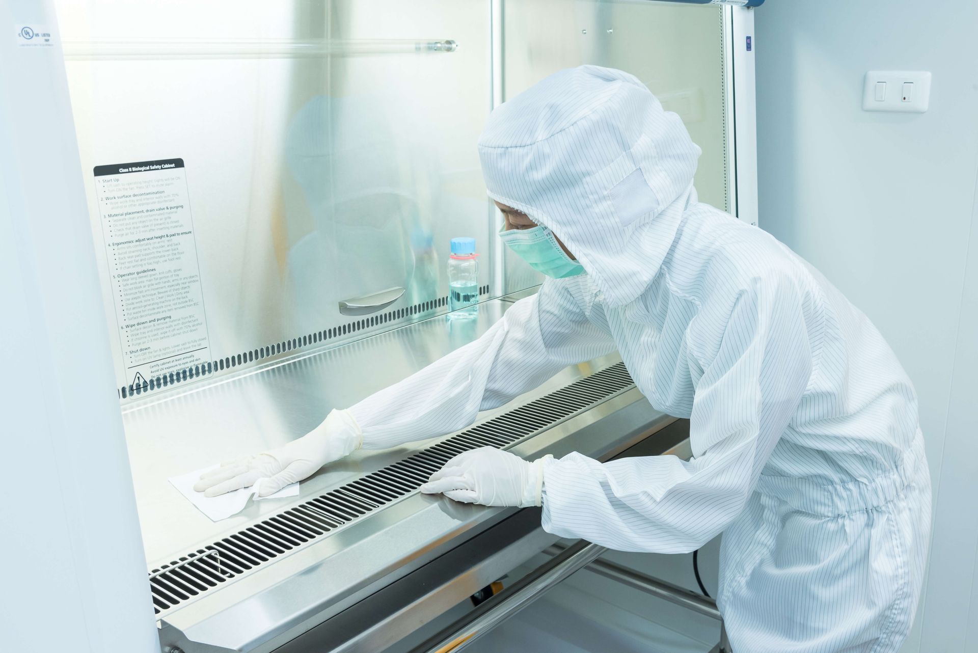 Person in protective suit cleaning a stainless steel laboratory cabinet.