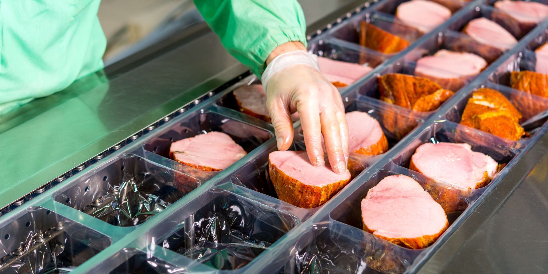 Person in protective gear placing meat portions into trays.