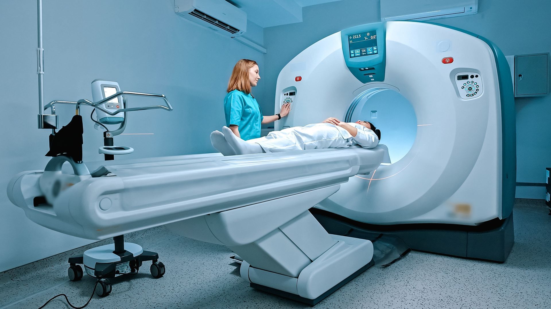 Medical staff assisting a patient during a CT scan. Blue-lit scanner, patient on table, doctor at controls.