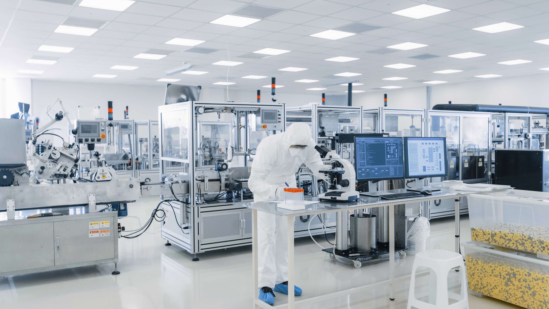 Scientist in protective suit working in a cleanroom lab with machines and monitors.