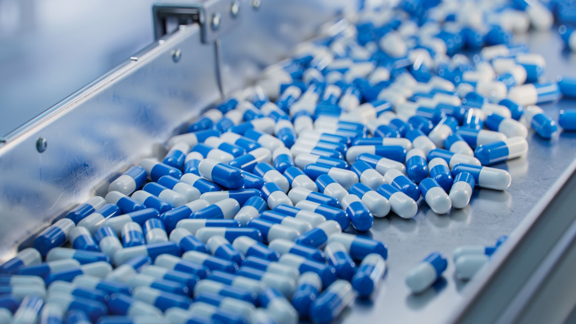 Blue and white capsules on a metal conveyor belt in a pharmaceutical factory.