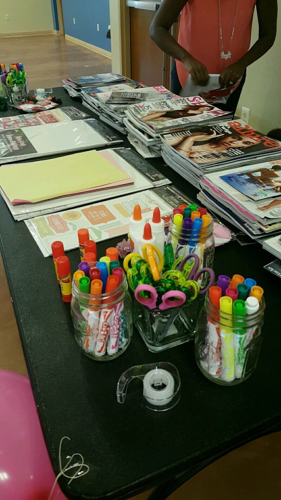 A table topped with jars of markers , scissors , glue and magazines.