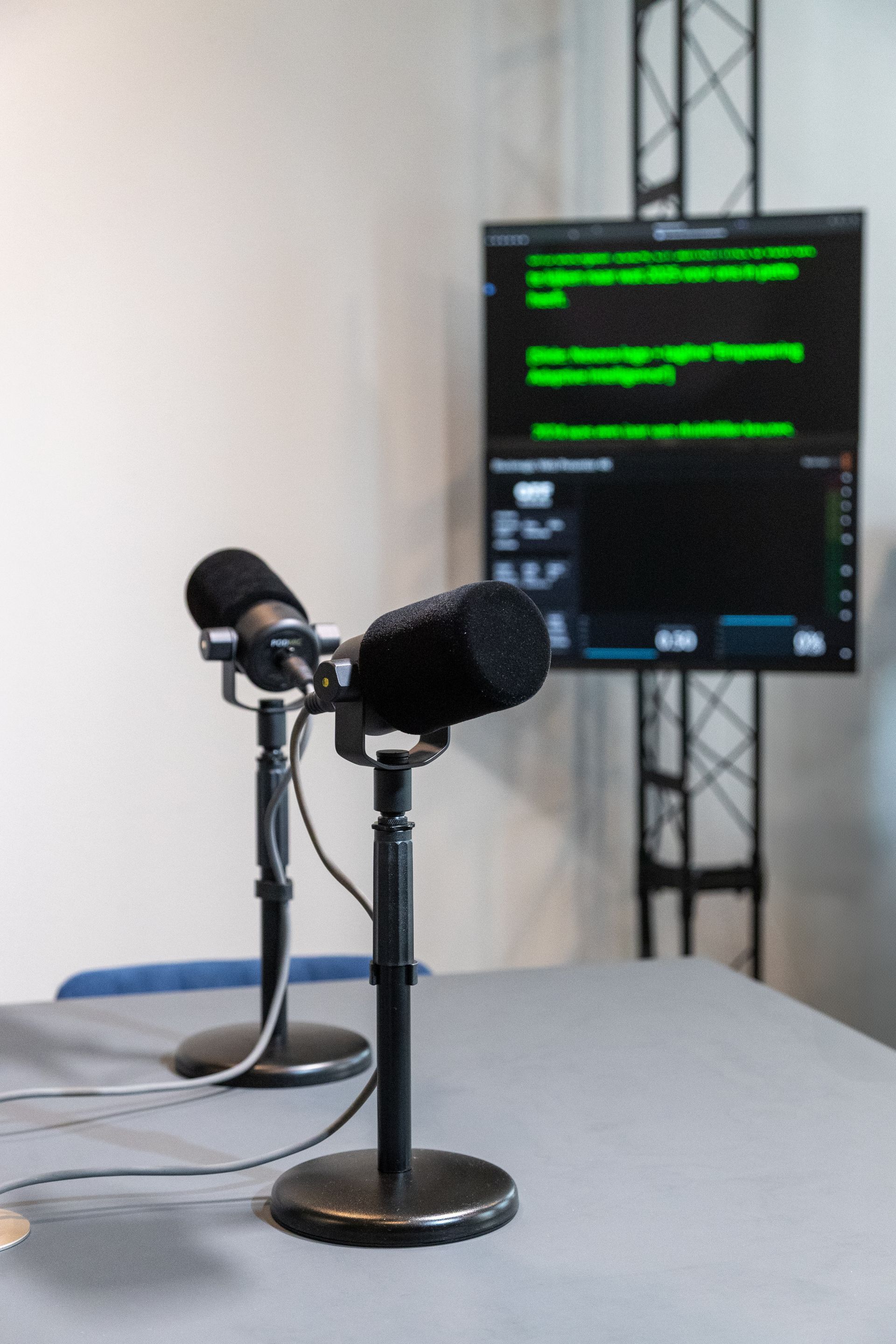 Twee microfoons op standaards staan voor een monitor met tekst op een tafel in een studio.