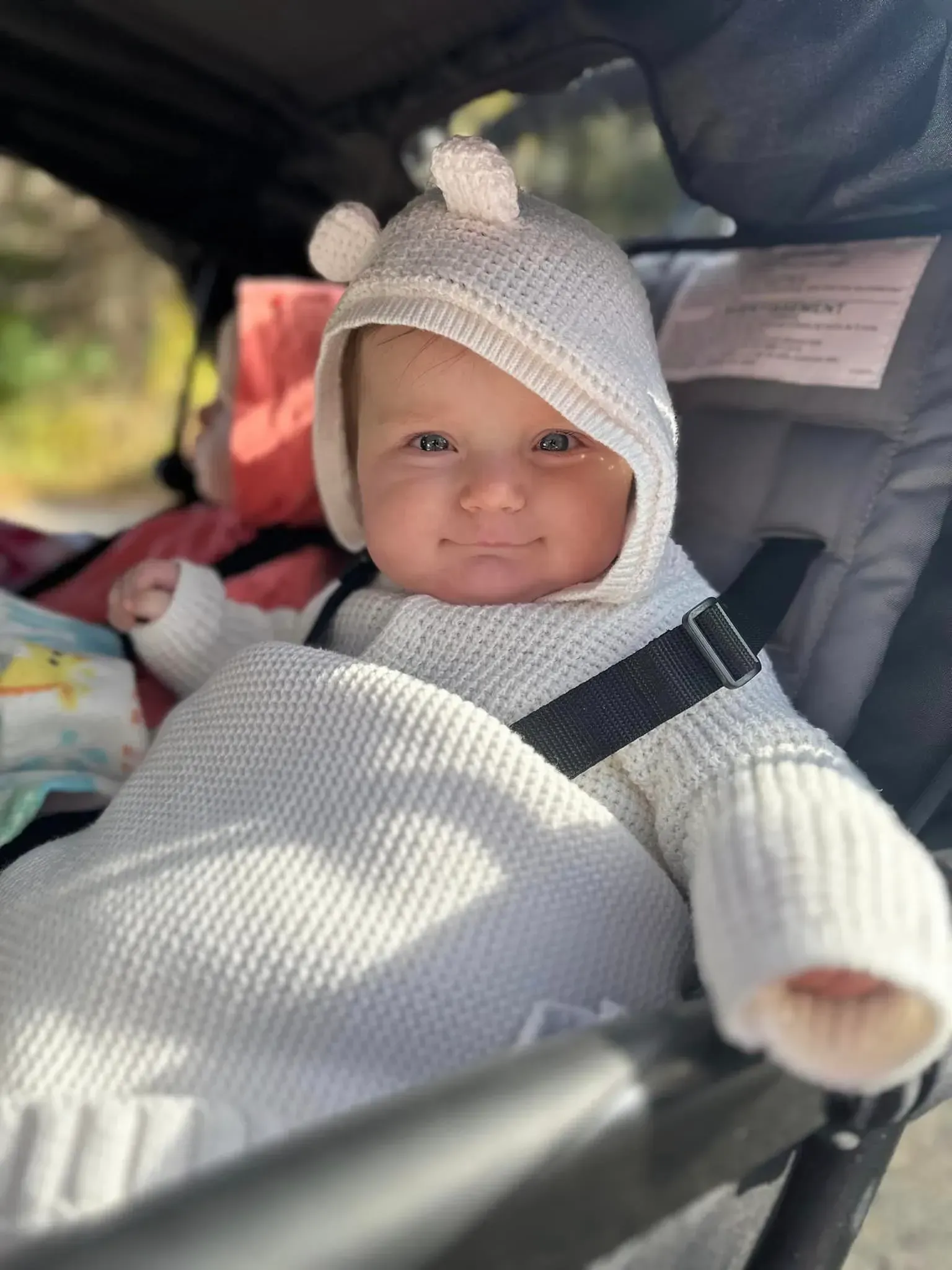 A baby wearing a white hat is sitting in a stroller.