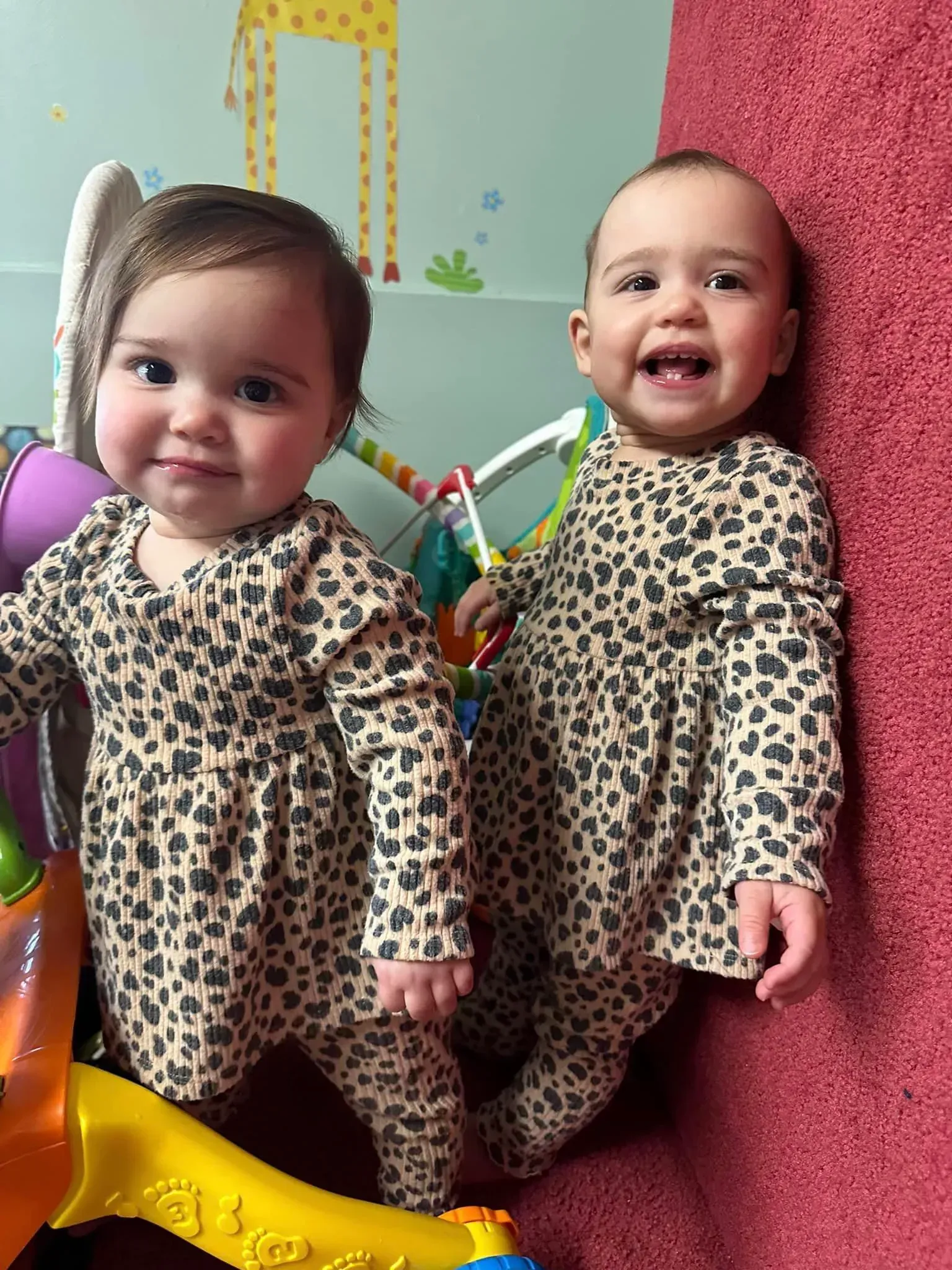 Two baby girls wearing leopard print dresses are standing next to each other.