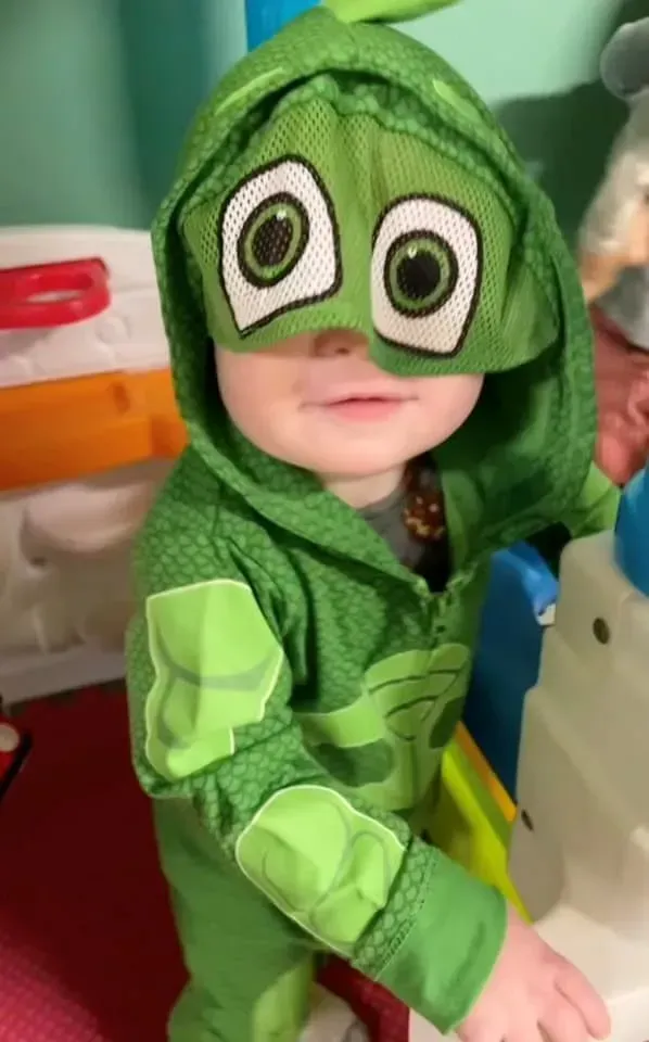 A baby is wearing a green costume and mask.