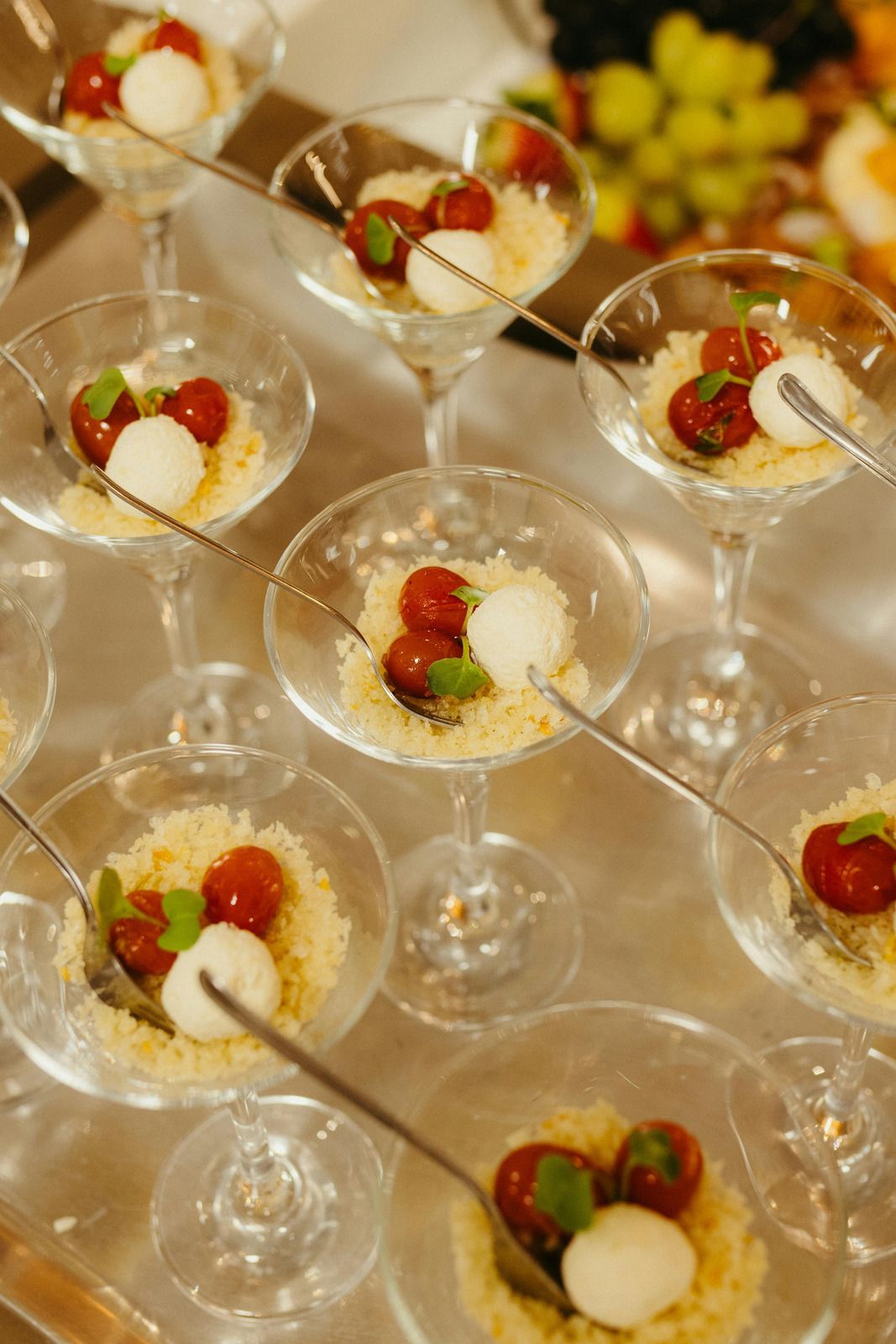 Several martini glasses filled with couscous, cherry tomatoes, and mozzarella balls arranged on a tray.