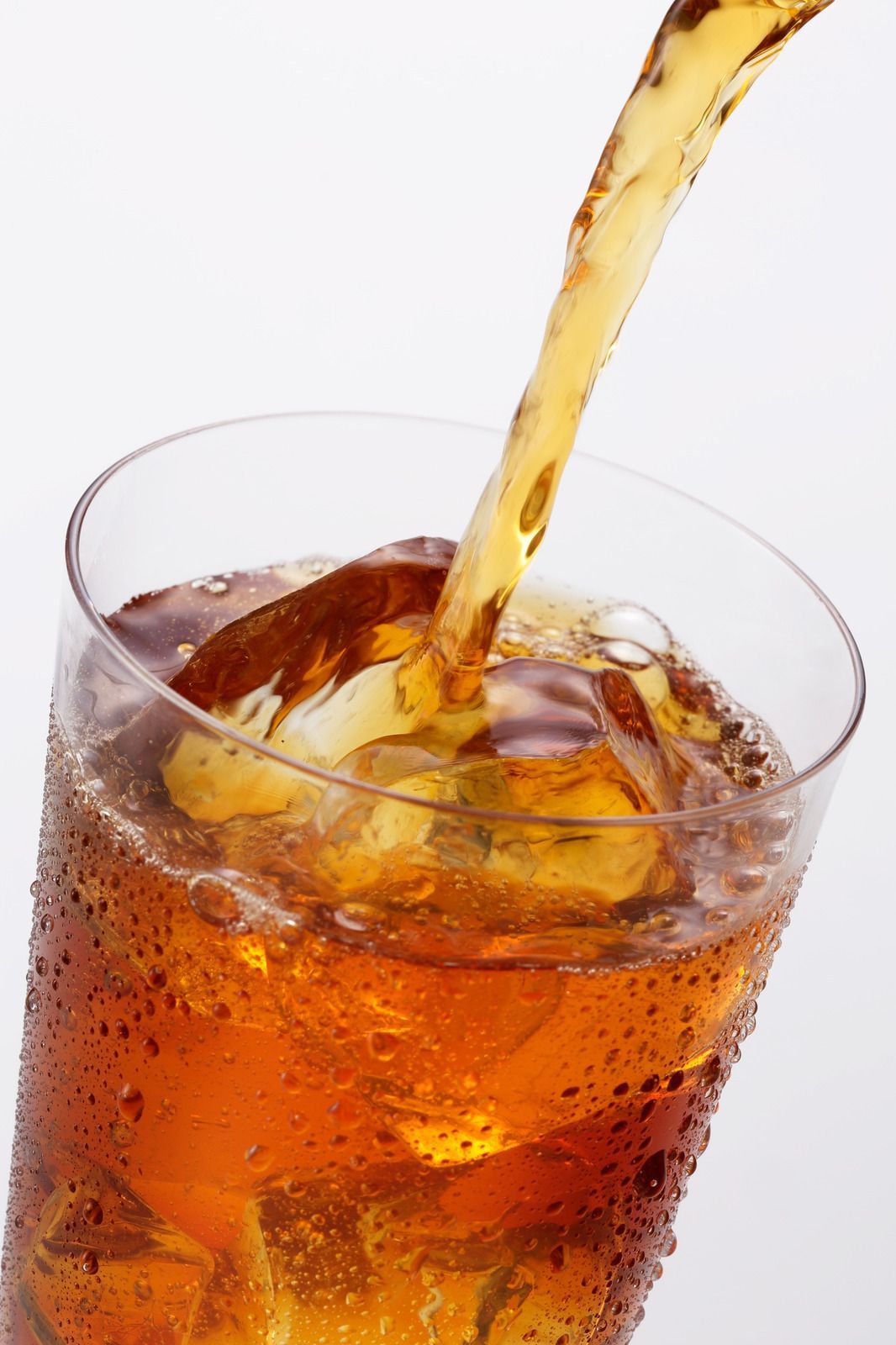 Amber-colored iced tea is being poured into a tall, condensation-covered glass filled with ice cubes.
