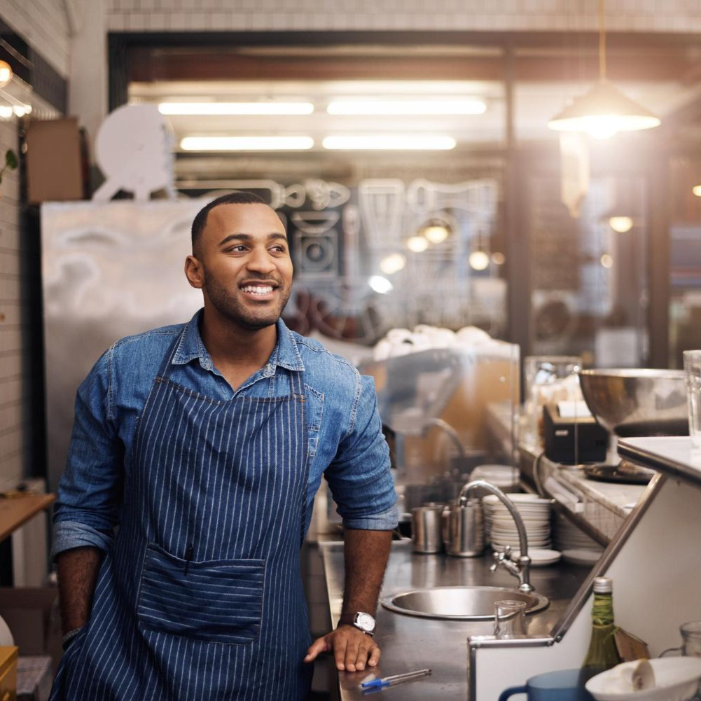 Barista smiling behind a café counter in a blue striped apron
