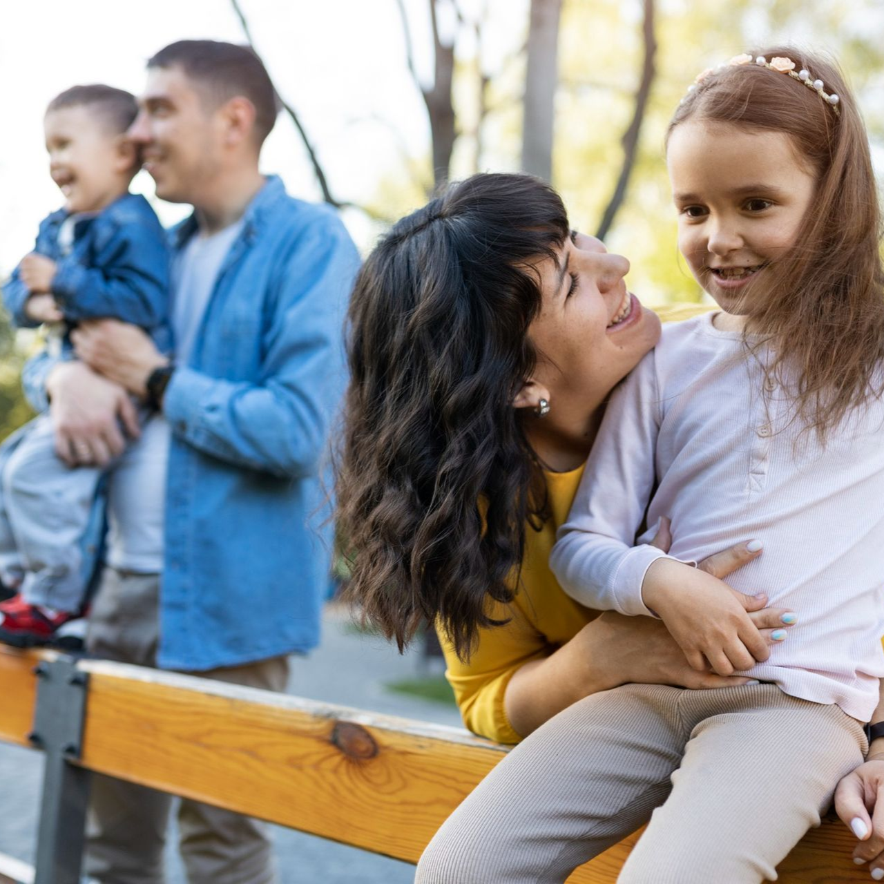 Two adults and two children sitting and smiling on a park bench outdoors