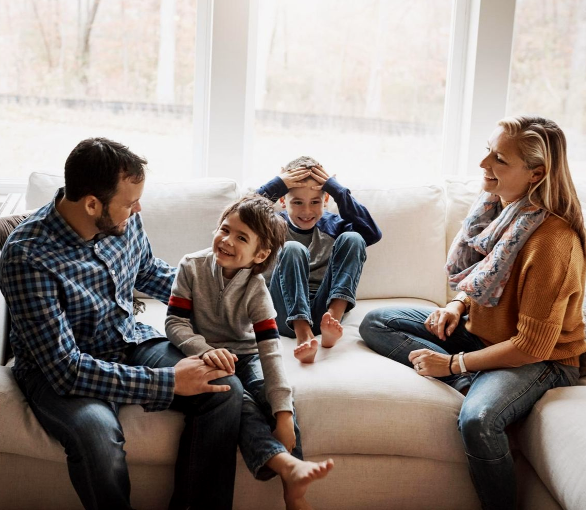 Family sitting together on a couch in a bright living room, smiling and talking