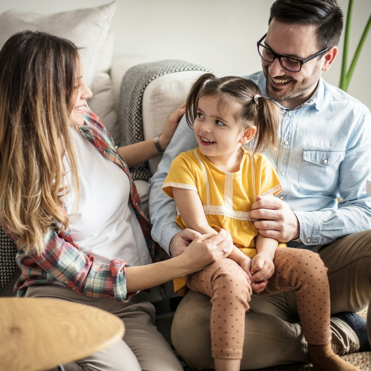 Family sitting on a couch, smiling and chatting with a young child in a yellow shirt